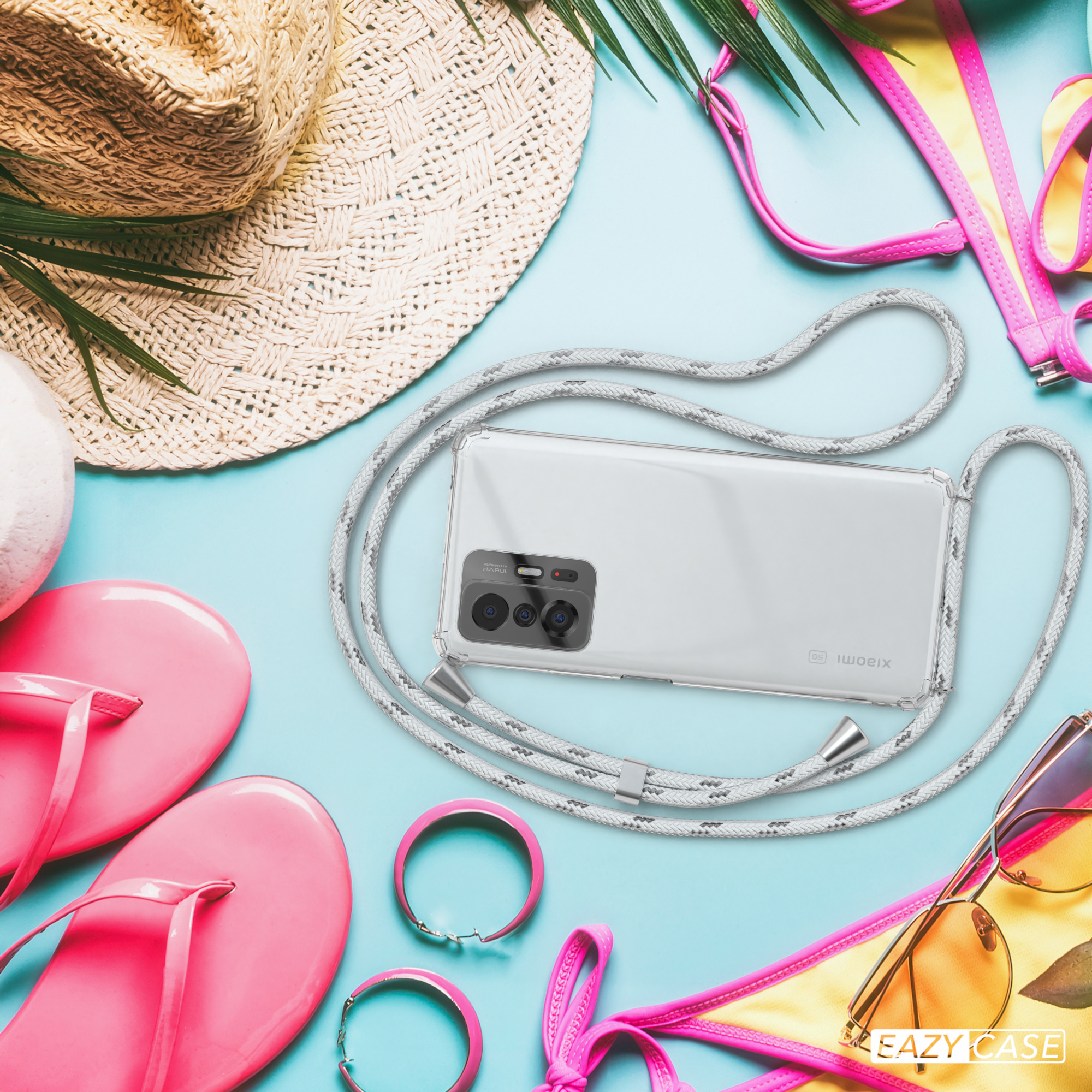 Telefon in klarer Hülle mit Band, auf blauem Untergrund mit Sommeraccessoires: Hut, Sonnenbrille, Flip-Flops.