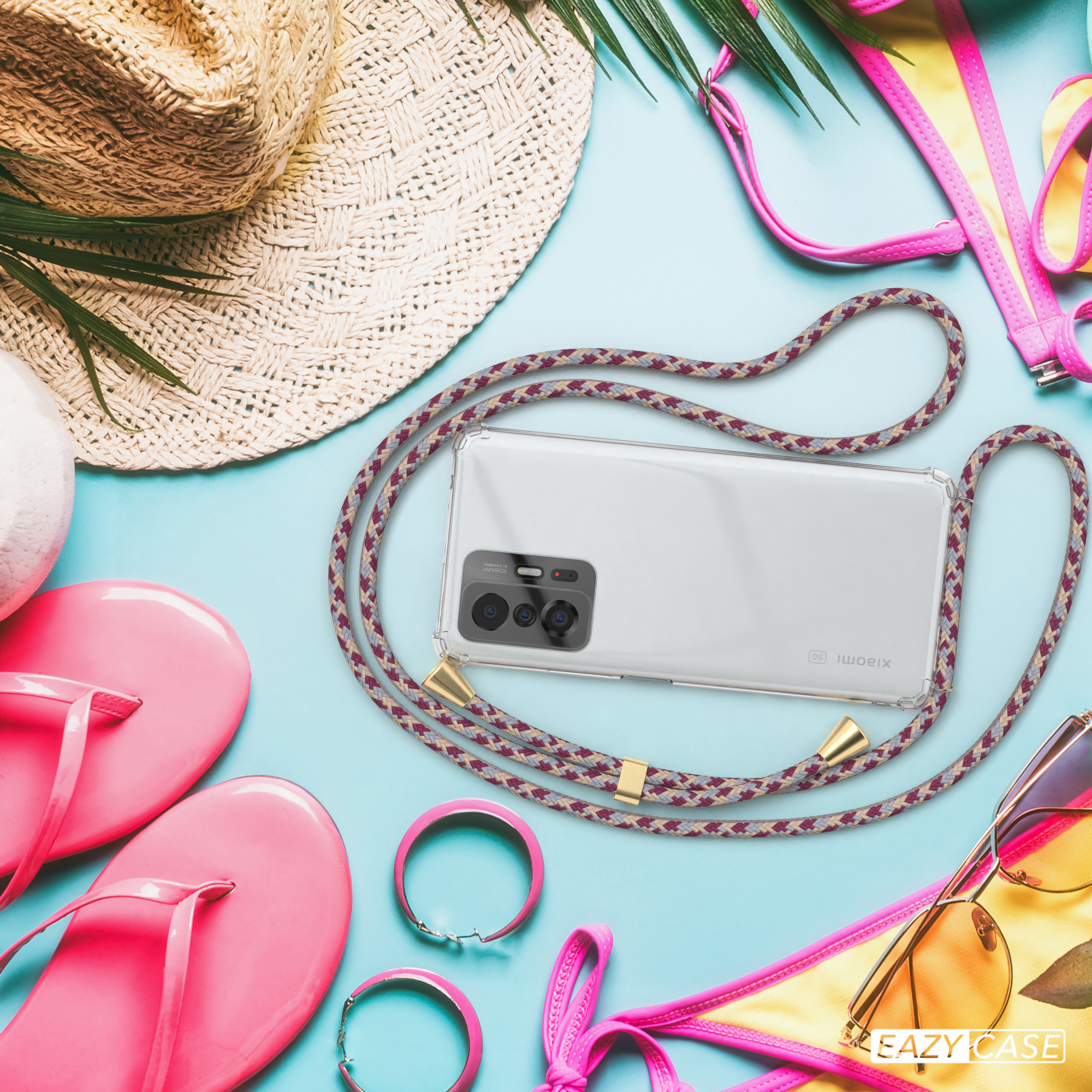 Telefon in transparenter Hülle mit Band auf blauem Untergrund mit Strandaccessoires. Band mit burgundfarbenem Muster.