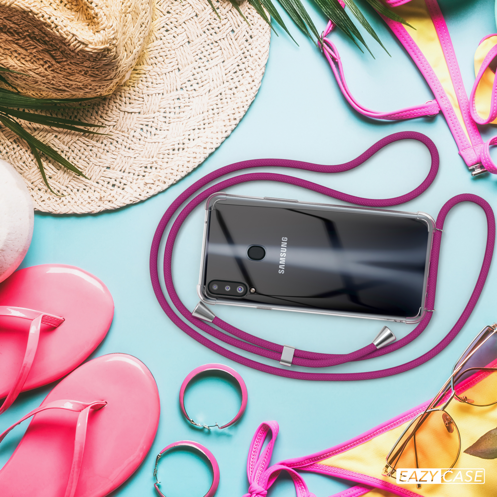 Telefon mit lila Umhängeband und Hülle, umgeben von Strandutensilien, einschließlich Hut.