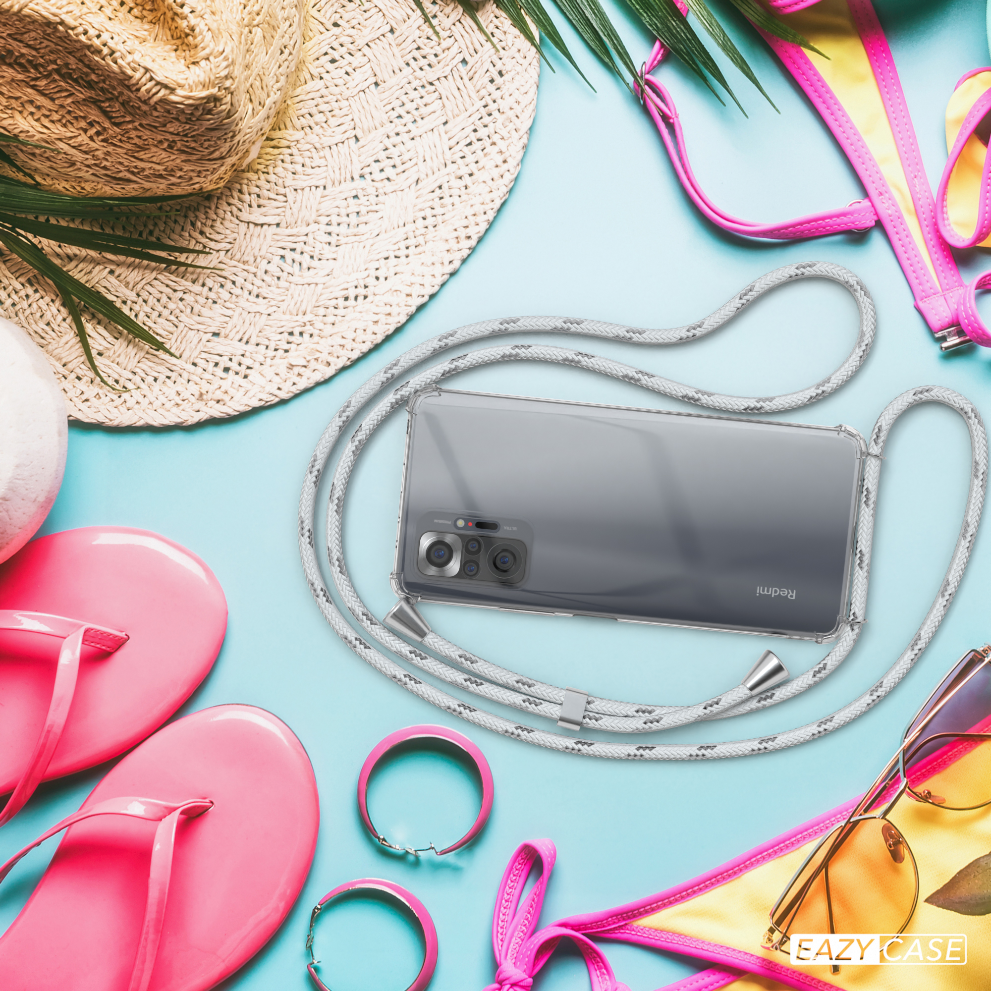 Telefon mit klarer Hülle und grauem Band. Strandszene mit Accessoires im Hintergrund.