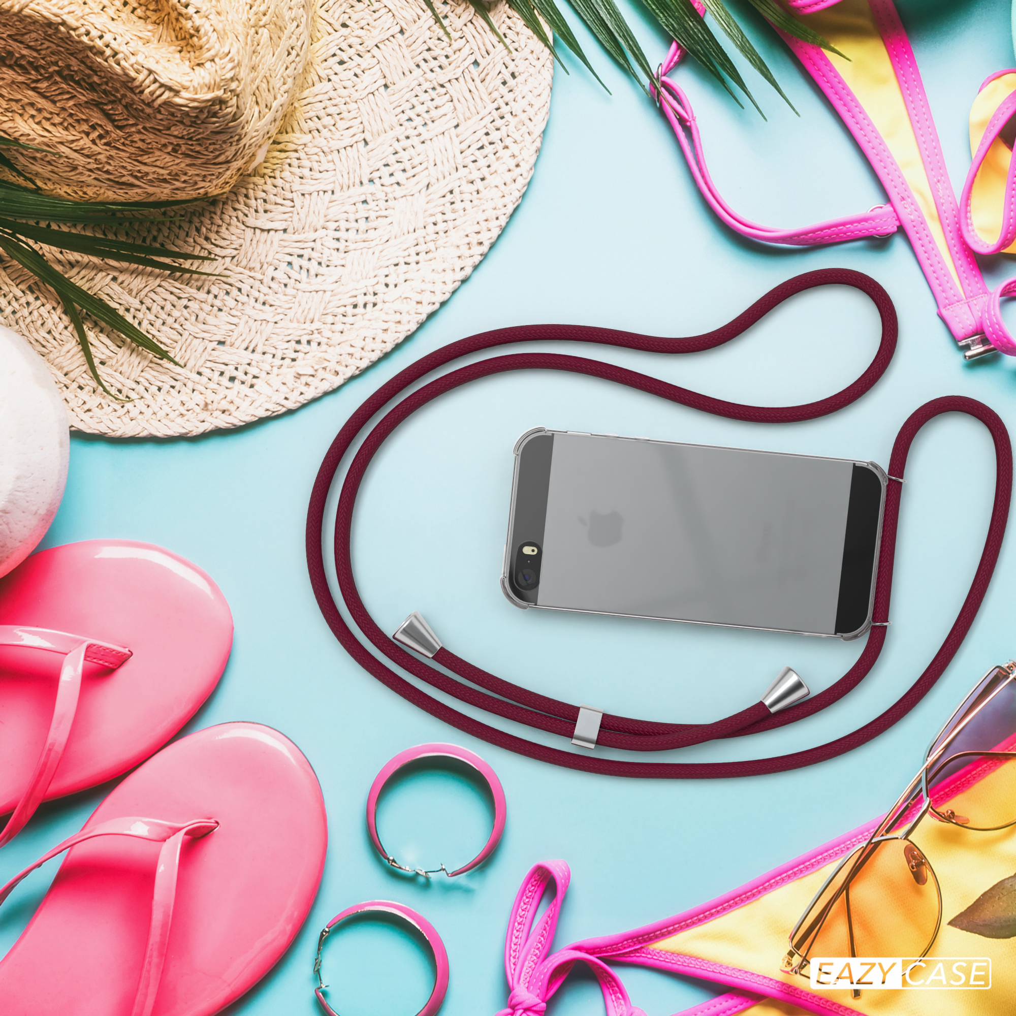 Ein Telefon mit bordeauxfarbenem Kabel liegt auf blauem Grund, umgeben von Sommeraccessoires.