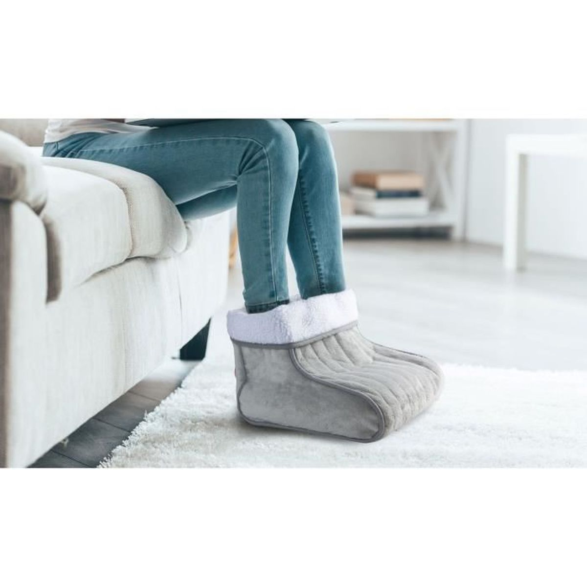 Una persona con i jeans blu è seduta su un divano grigio, indossando una pantofola riscaldata grigia.