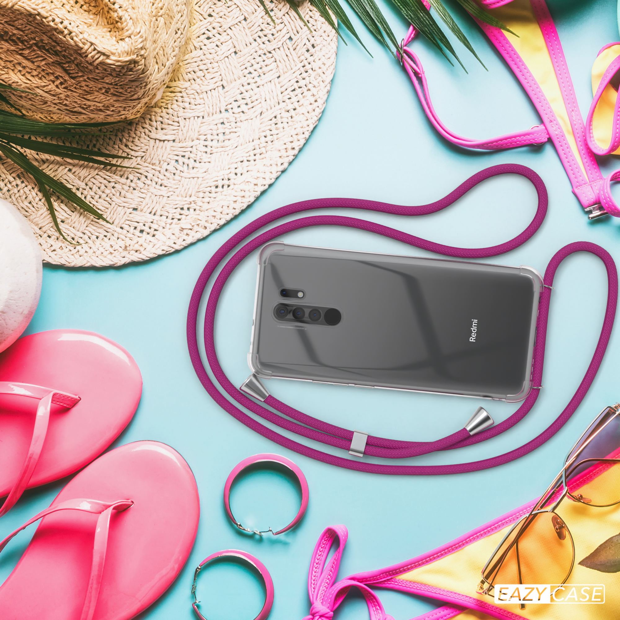 Ein Telefon mit magenta Kabel liegt auf blauer Oberfläche. Sommerartikel wie Sonnenbrille und Bikinioberteil sind in der Nähe.