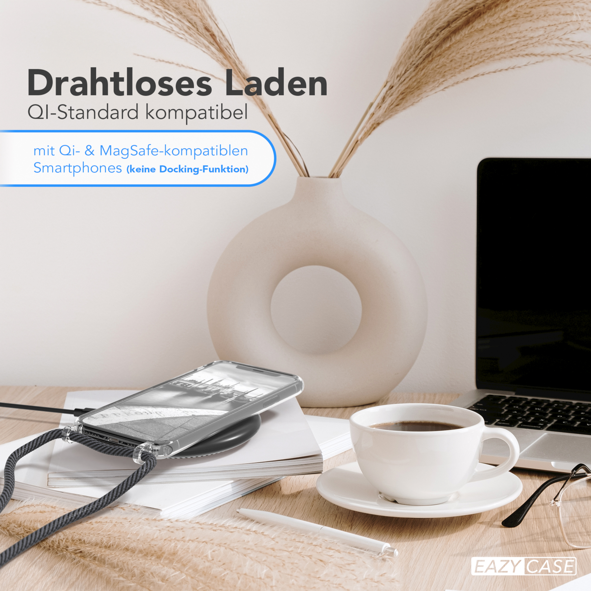 Telefon auf kabellosem Ladegerät, mit Tasse und Blumen. Laptop im Hintergrund.