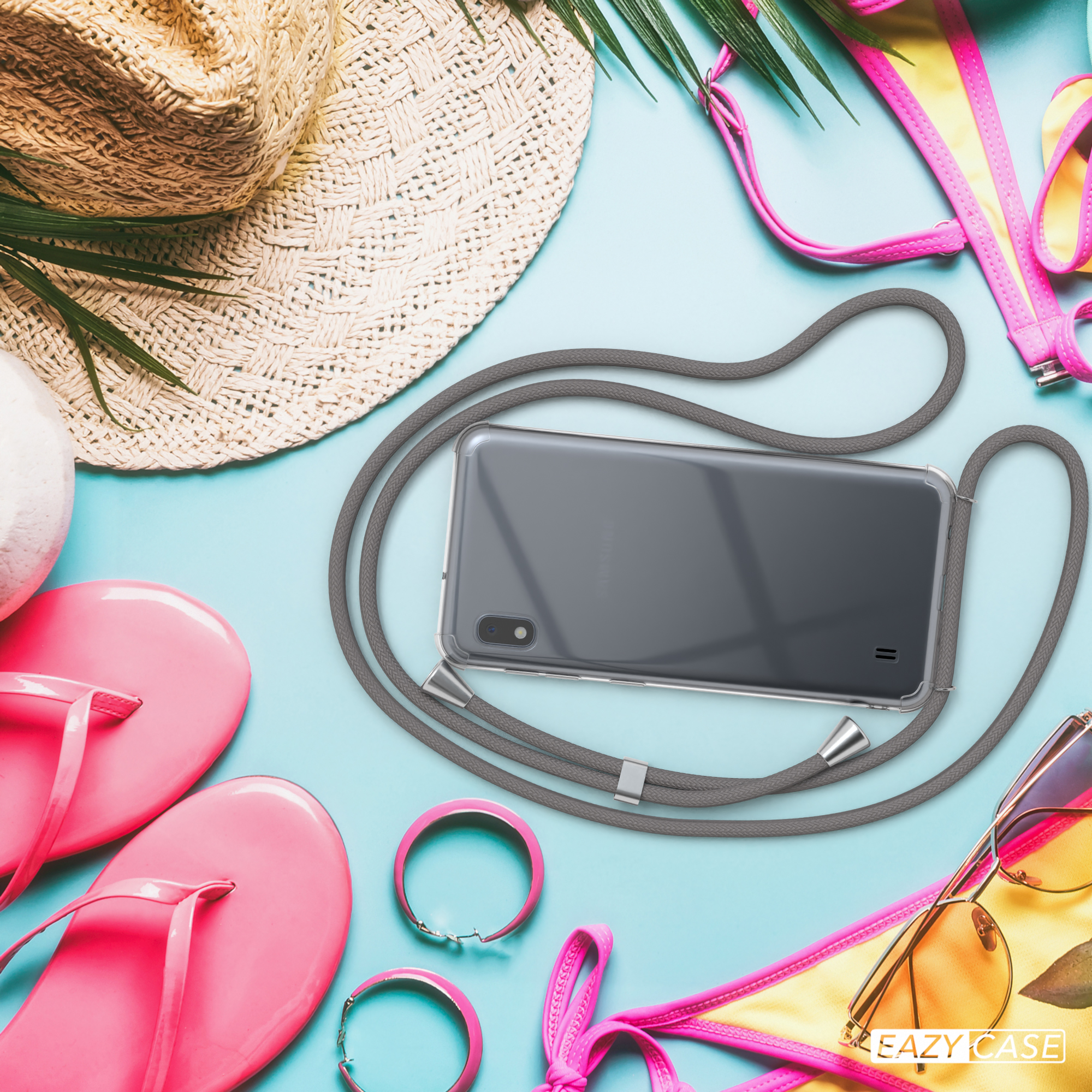 Telefon mit grauem Umhängeband, umgeben von Strandaccessoires: Hut, Flip-Flops, Sonnenbrille und Bikini-Oberteil.