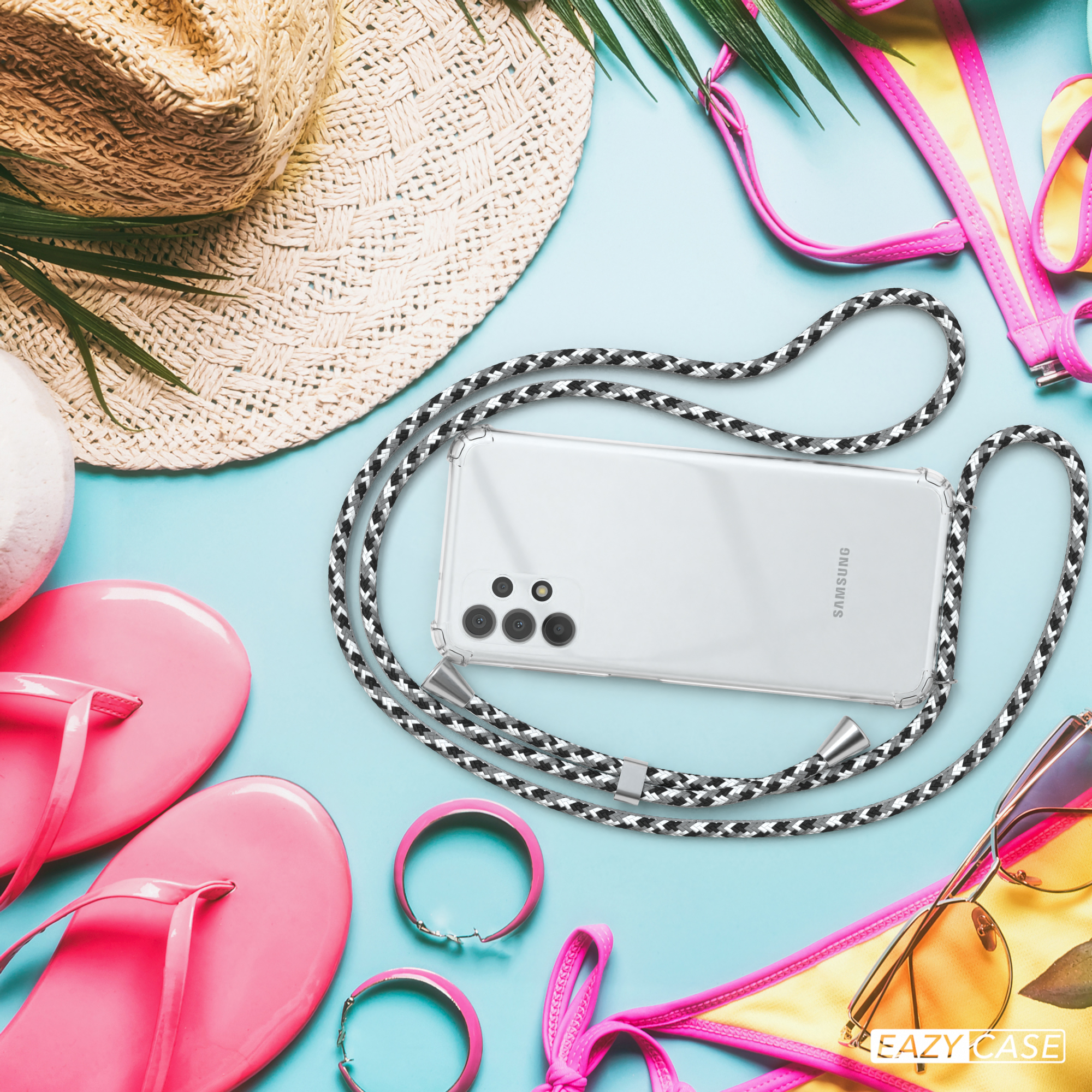 Strandszene mit Telefon an einem schwarz-weißen Lanyard, neben Strandaccessoires wie Hut und Sonnenbrille.