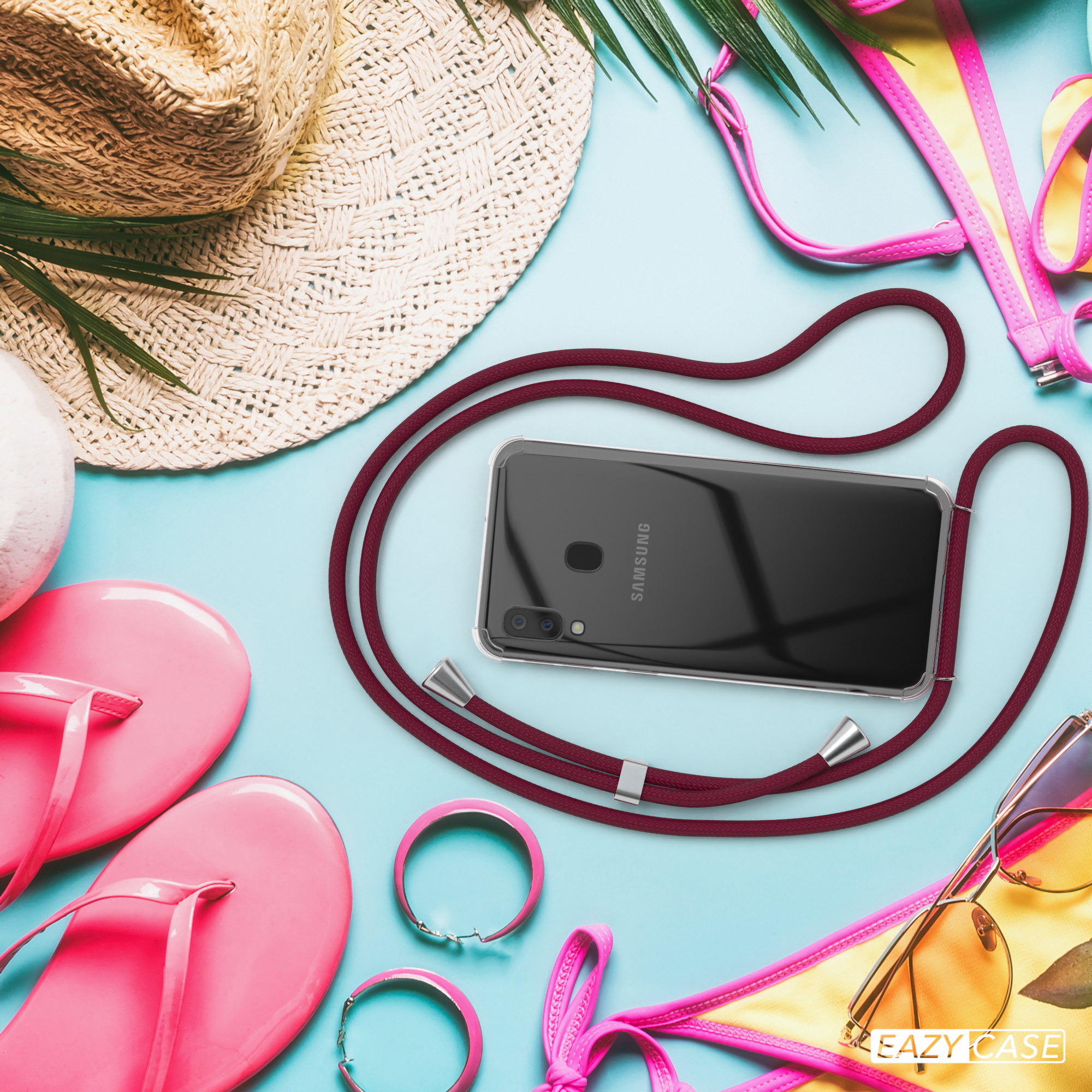Strandszene mit Telefon an einem roten Lanyard, mit Strandaccessoires wie Hut, Flip-Flops und Sonnenbrille.