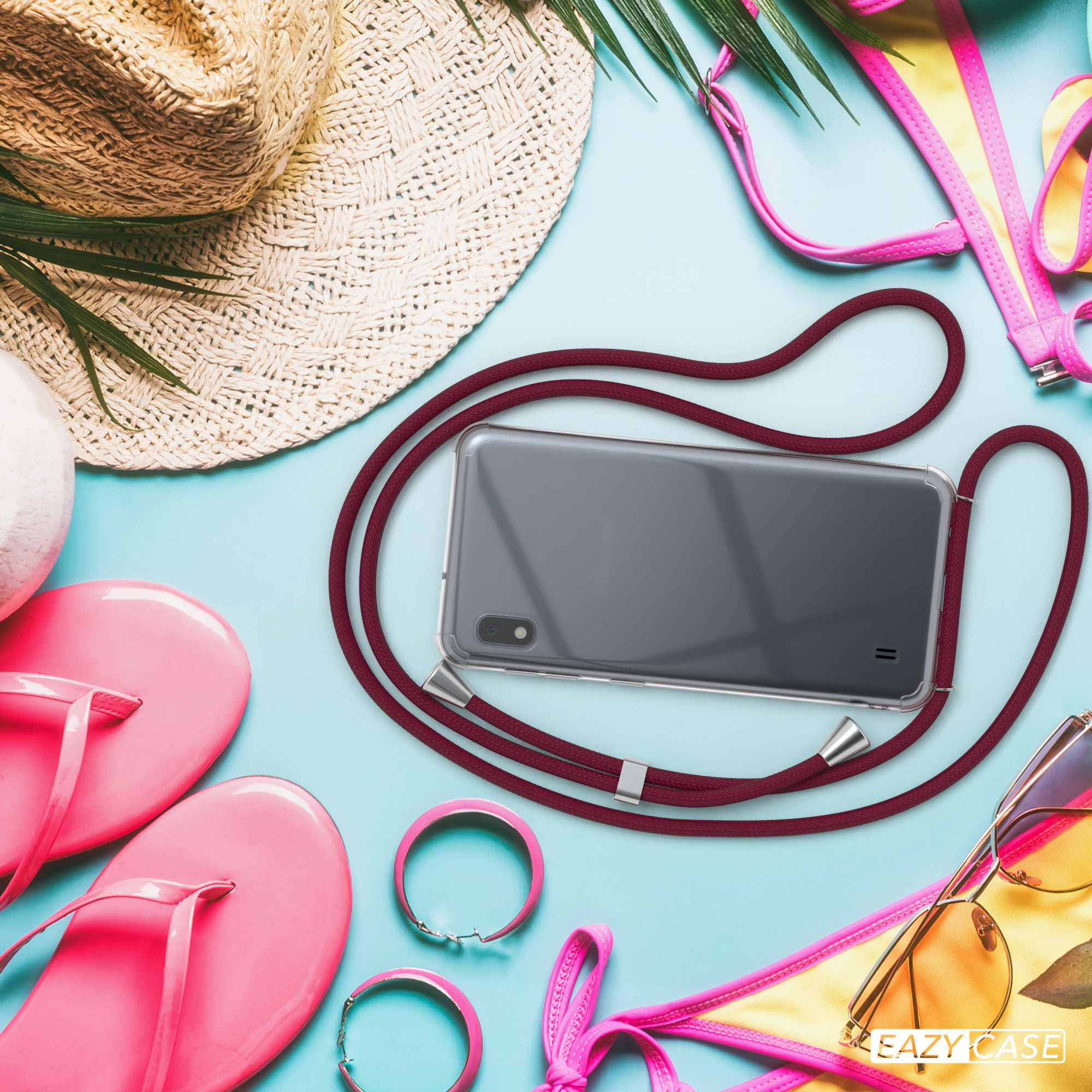 Ein Telefon mit roter Kordel, Strandutensilien auf blauem Grund, ein Hut, Sandalen und ein Bikini.