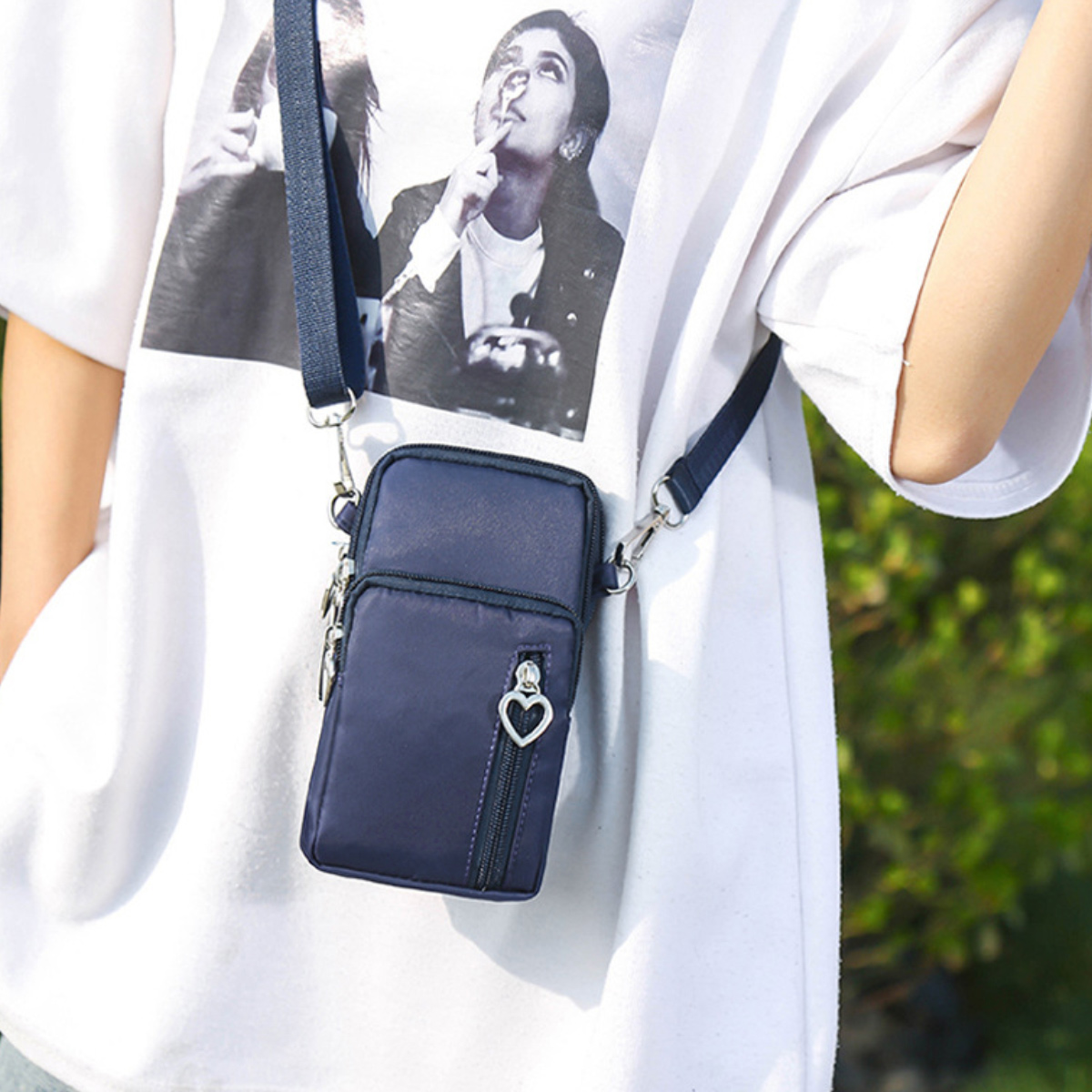 Person trägt weißes Hemd. Navy-Handytasche mit herzförmigem Reißverschluss.