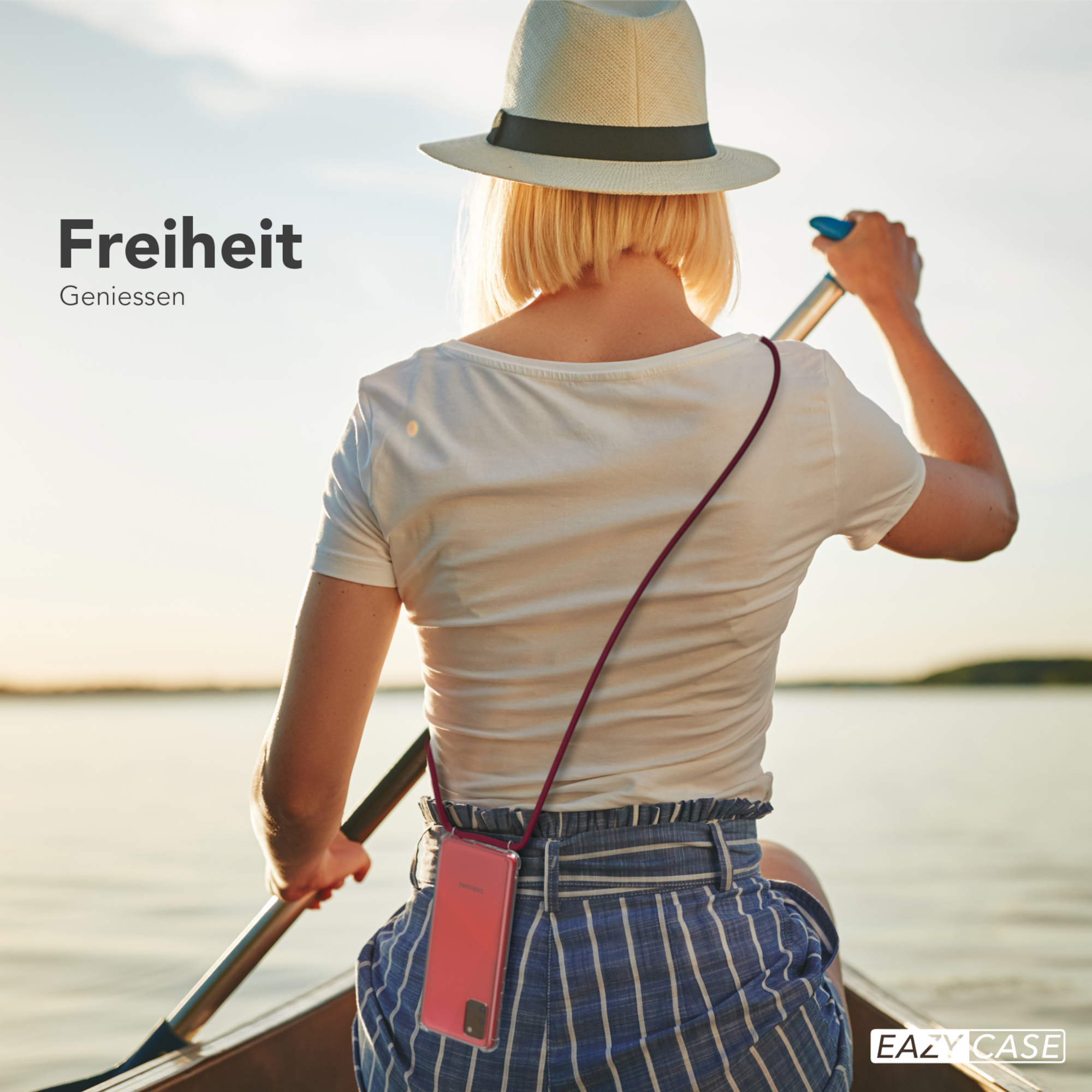 Frau im Hut rudert ein Boot mit einer Handyhülle um den Hals. Sonne und Wasser im Hintergrund. Text: Freiheit.