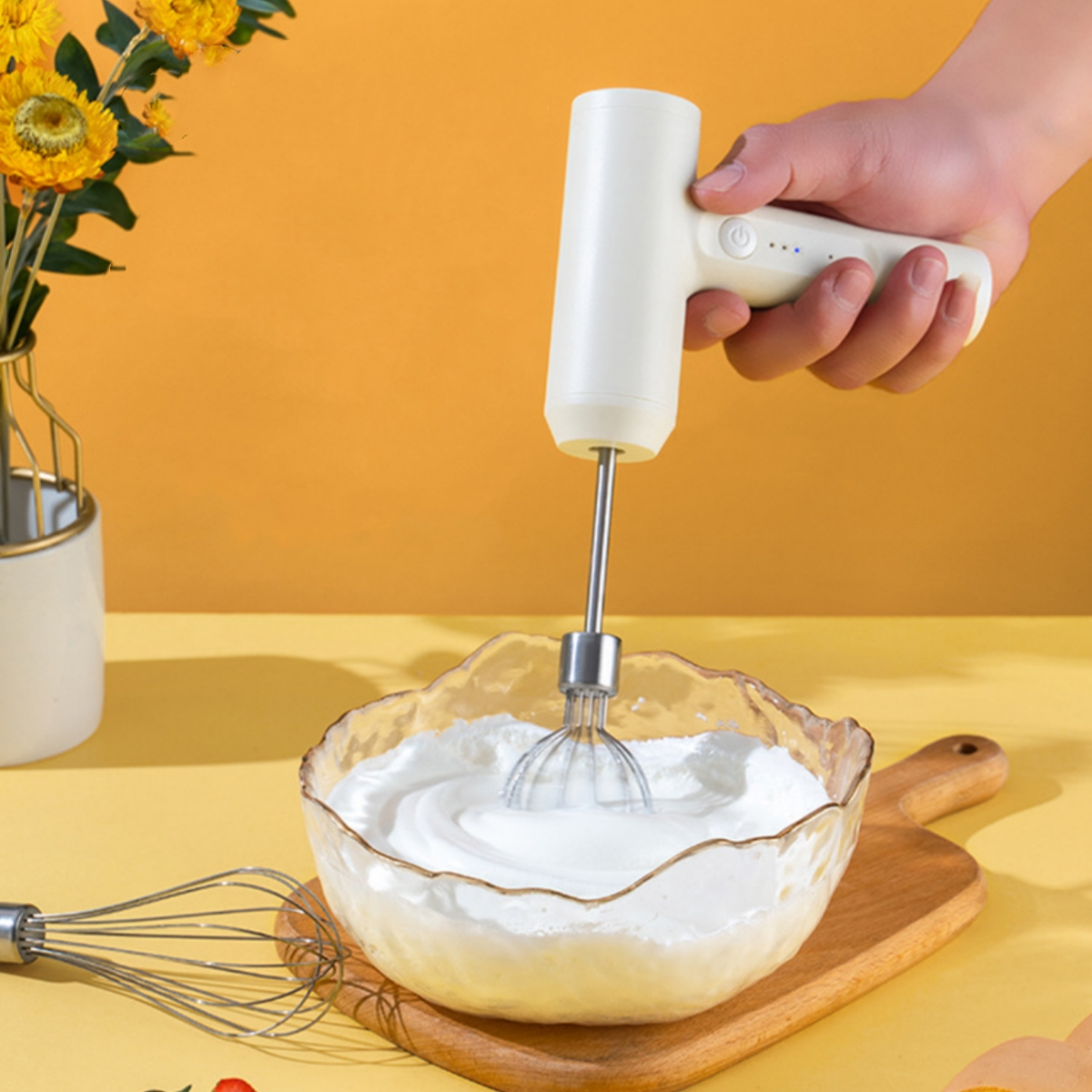 Hand hält einen weißen elektrischen Mixer, der weiße Sahne in einer Glasschüssel auf Holz mischt.