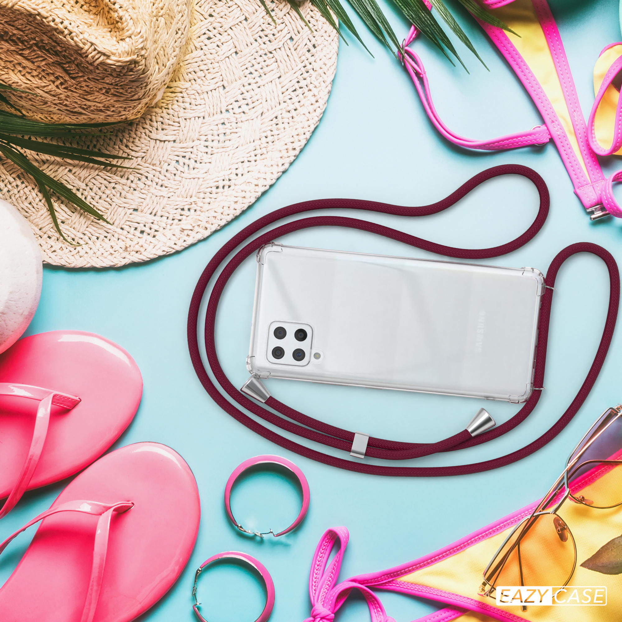 Ein Telefon in einer durchsichtigen Hülle mit einem weinroten Kabel liegt zwischen Strandaccessoires.
