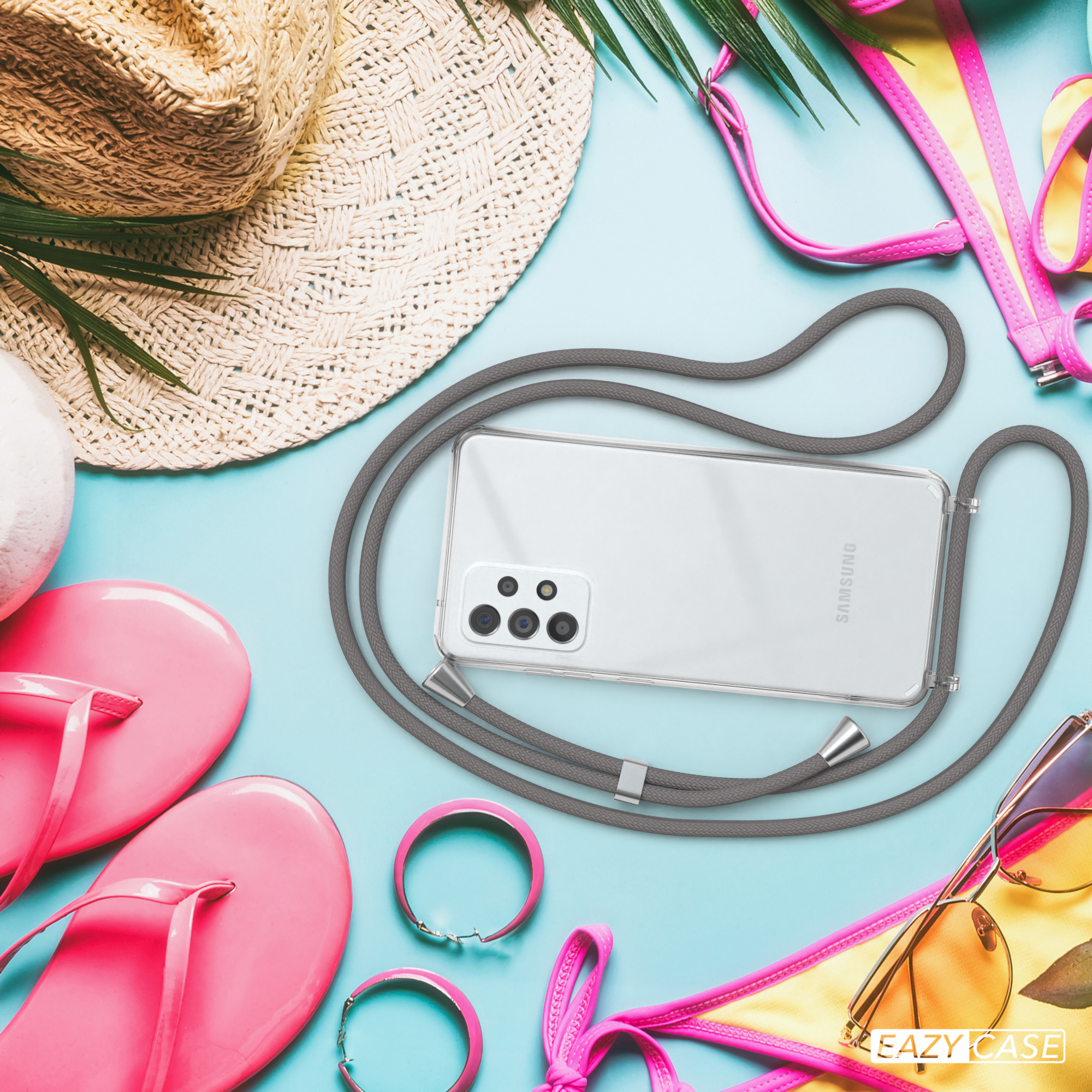 Telefon mit Gurt liegt auf Strandartikeln: Hut, Sonnenbrille, Flip-Flops, Bikini.