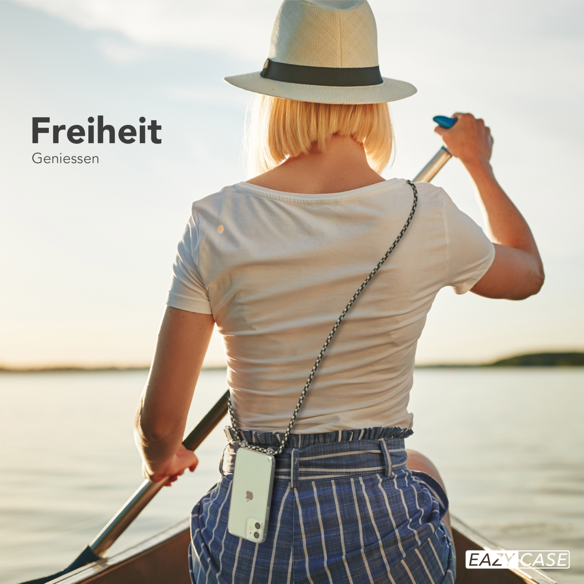 Frau paddelt in einem Boot, trägt einen Hut und ein Handy mit Umhängeband, bei Sonnenuntergang auf dem See.