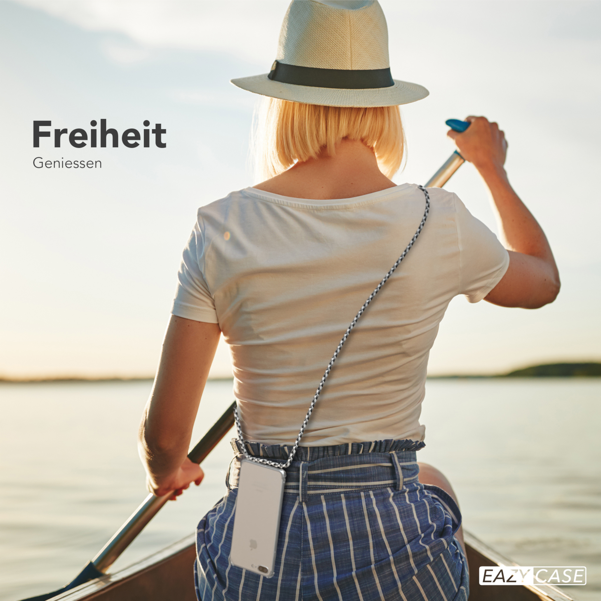 Eine Frau rudert ein Kanu auf einem See, trägt einen Hut und hält ein Ruder. Ein Telefon hängt um ihren Hals.