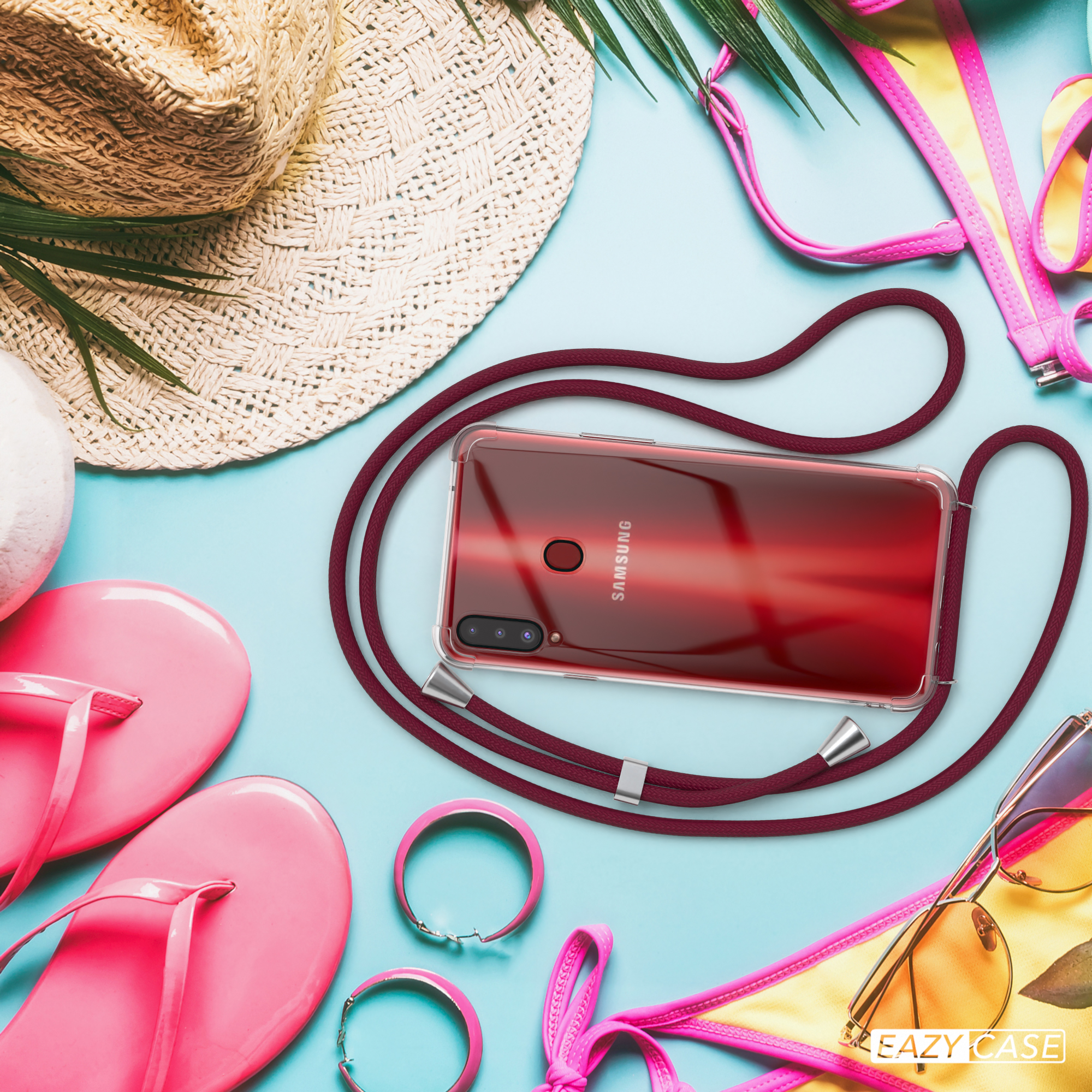 Telefon mit Band, Sonnenbrille, Hut und anderes Strandzubehör liegen auf einer blauen Oberfläche.
