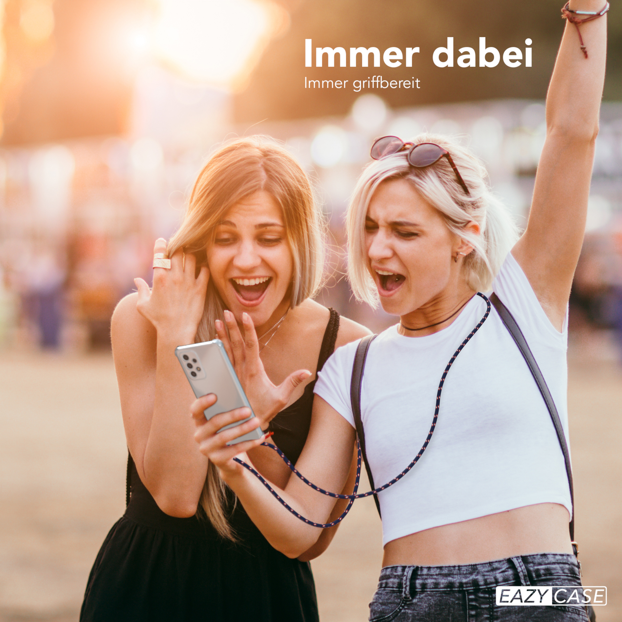 Zwei Frauen schauen auf ein Telefon. Eine trägt ein schwarzes Kleid, die andere ein weißes Top.