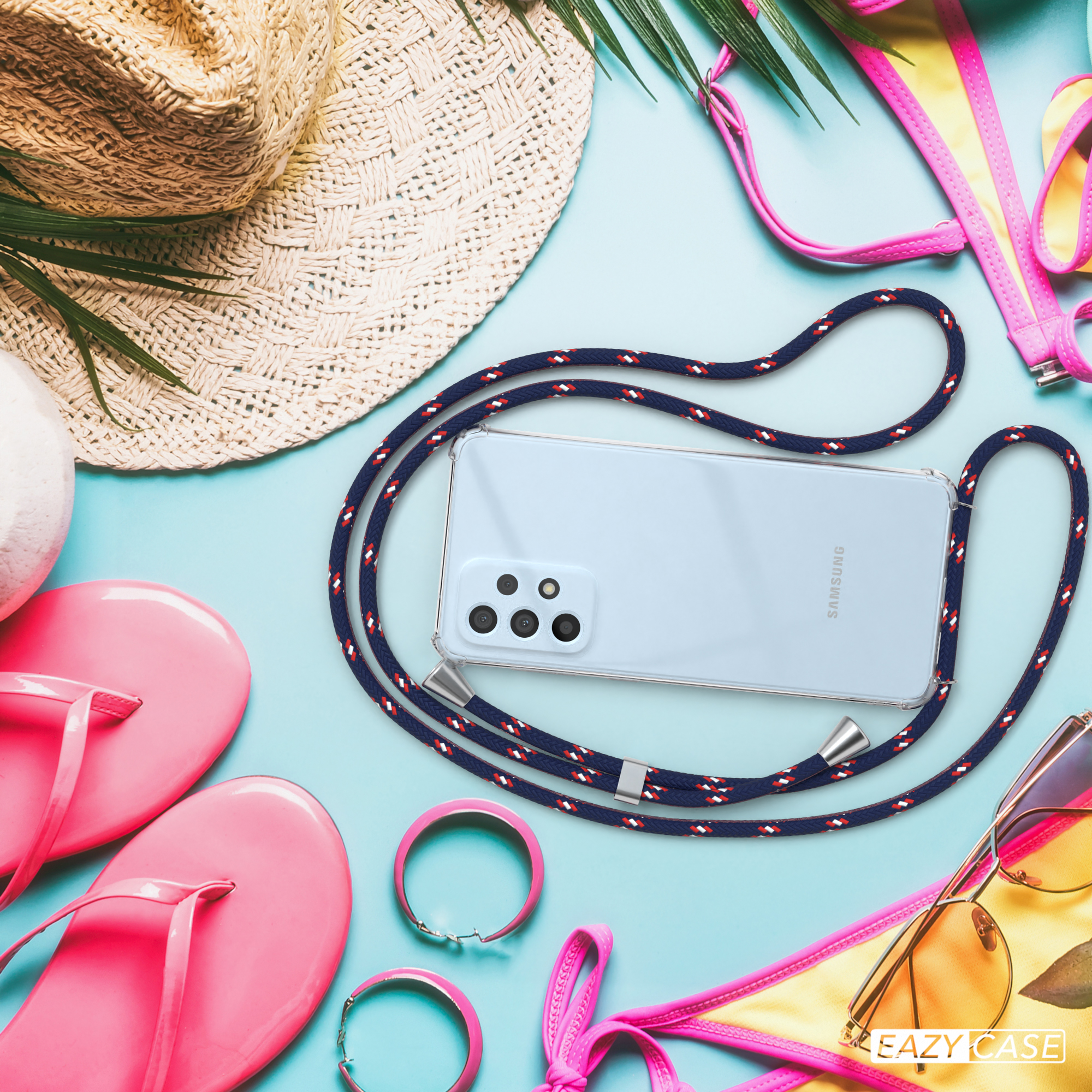 Ein Telefon mit Lanyard liegt auf blauem Untergrund mit Zubehör: Flip-Flops, Sonnenbrille, Armbänder.