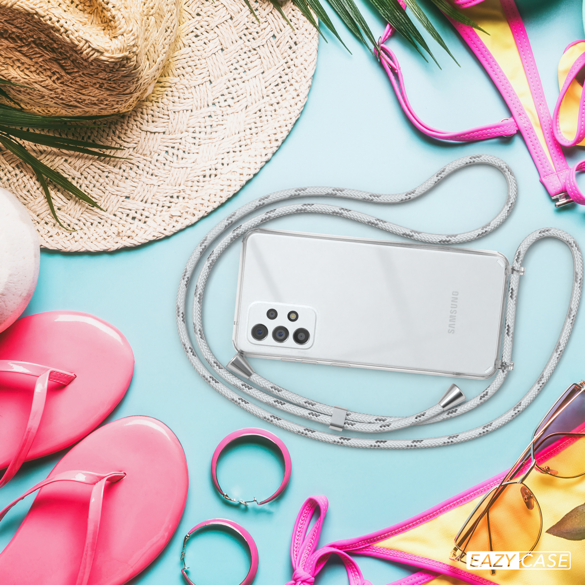 Telefon in transparenter Hülle mit grauem Kabel auf blauem Untergrund, Sonnenbrille und Strandmode.
