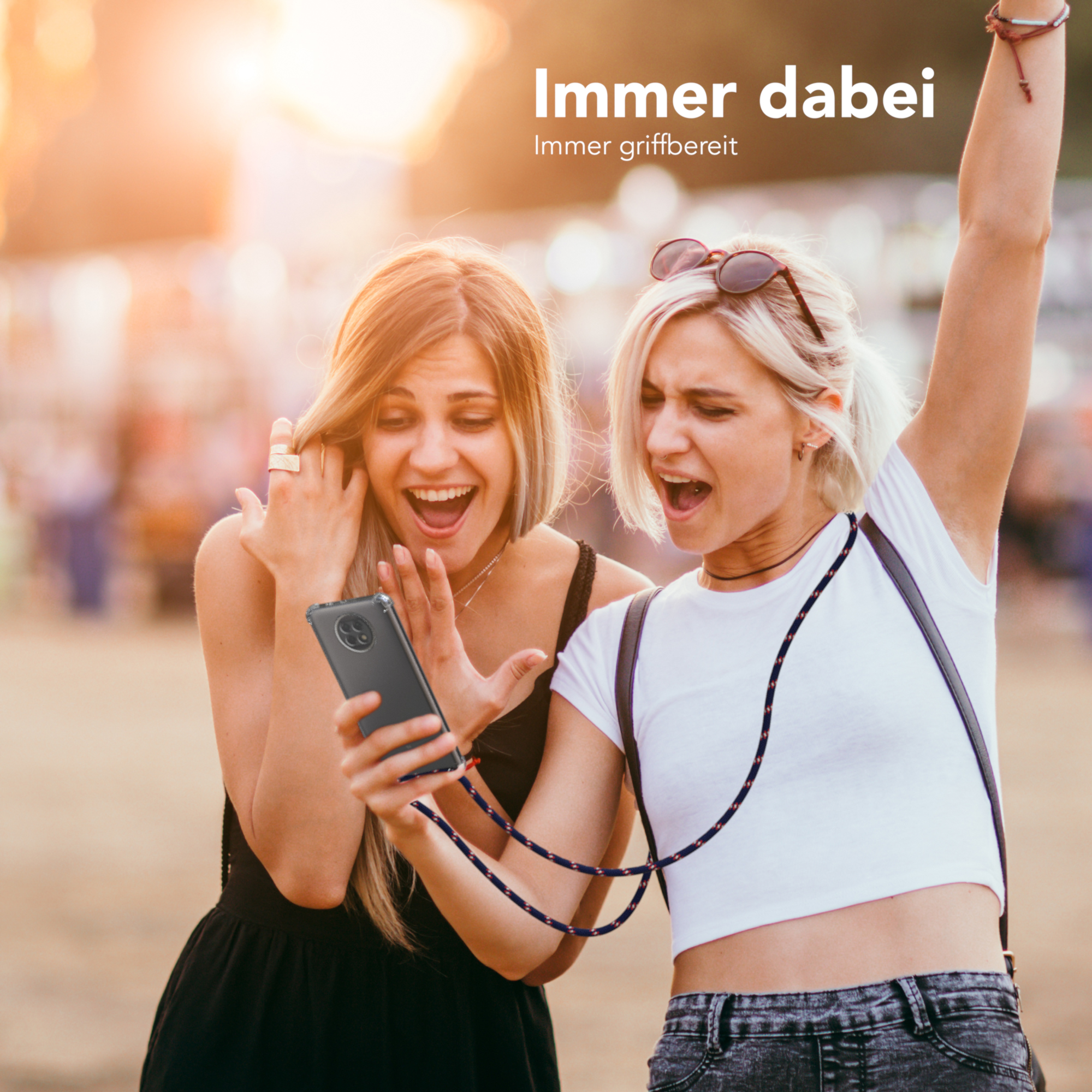 Zwei Frauen schauen auf ein Telefon. Eine mit einer Handyhülle um den Hals, lächelnd, die andere jubelnd.