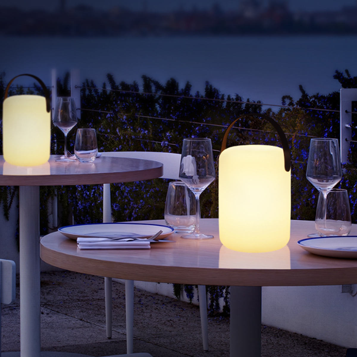 Zwei leuchtende Lampen auf einem Tisch, mit Gläsern und Blick aufs Wasser.