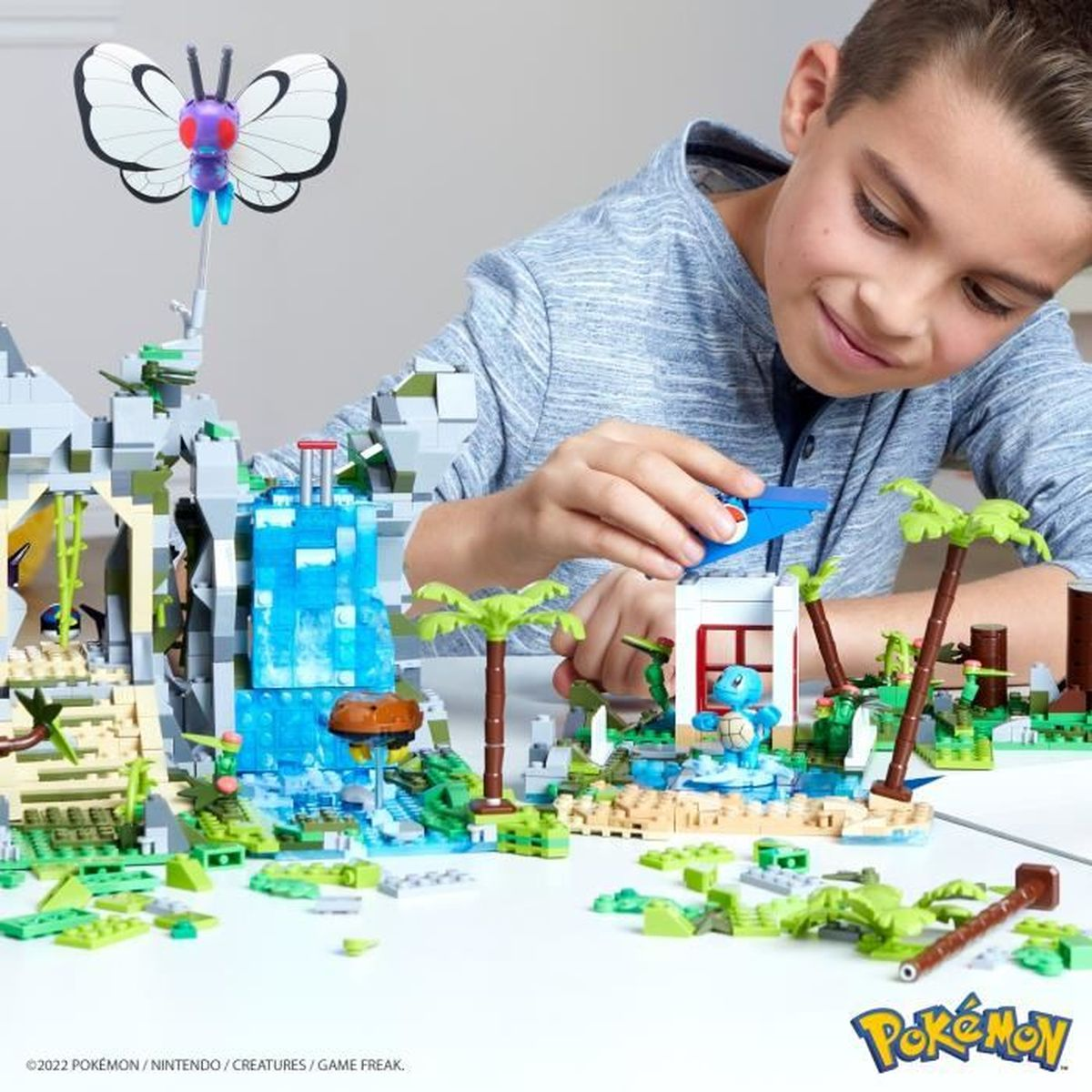 Ein Junge spielt mit einem Pokemon-Lego-Set, das eine Schiggy-Figur, einen Wasserfall und einen großen Schmetterling zeigt.