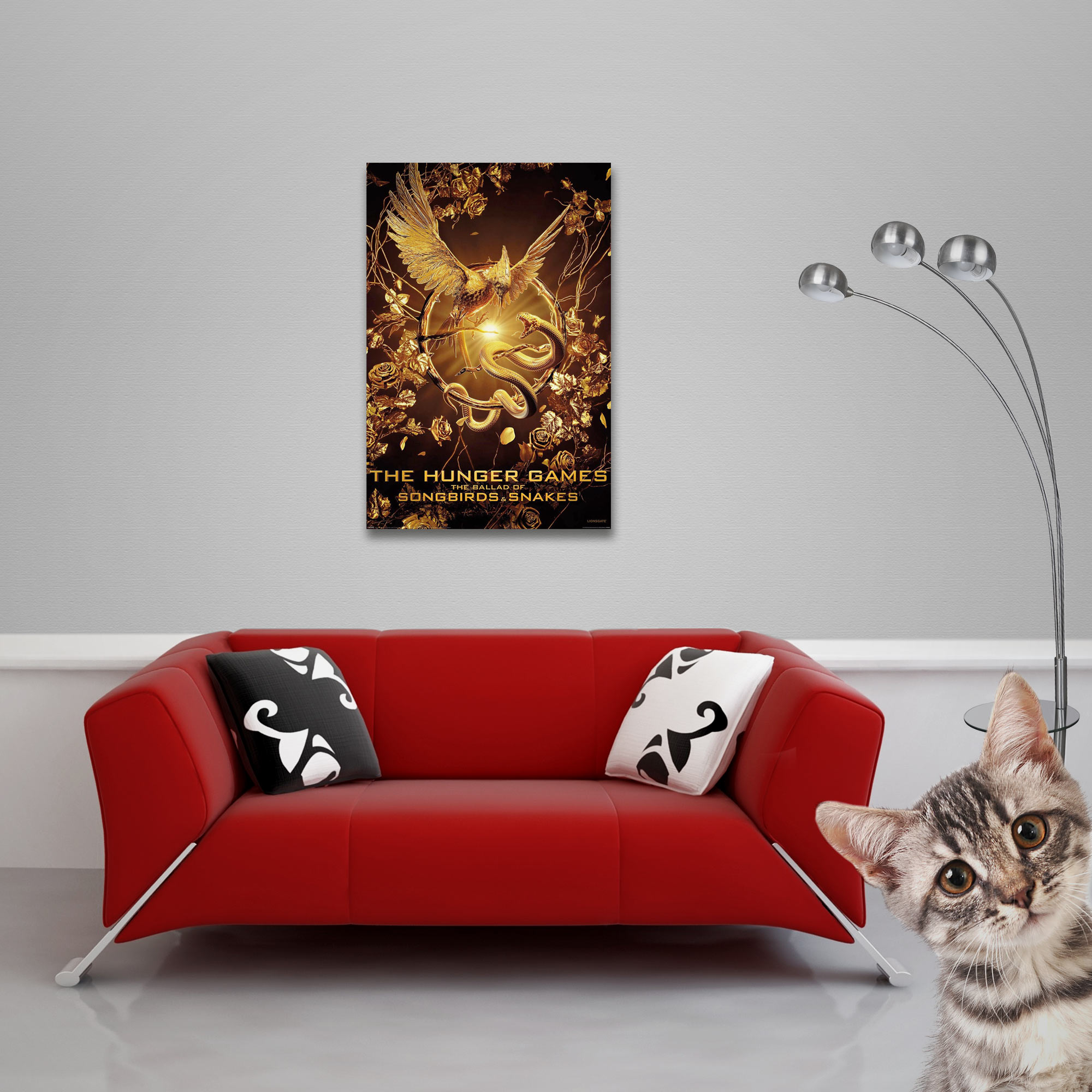 Ein Poster mit einem goldenen Vogel und einer Schlange. Ein rotes Sofa, eine Katze und eine Lampe sind ebenfalls im Bild.