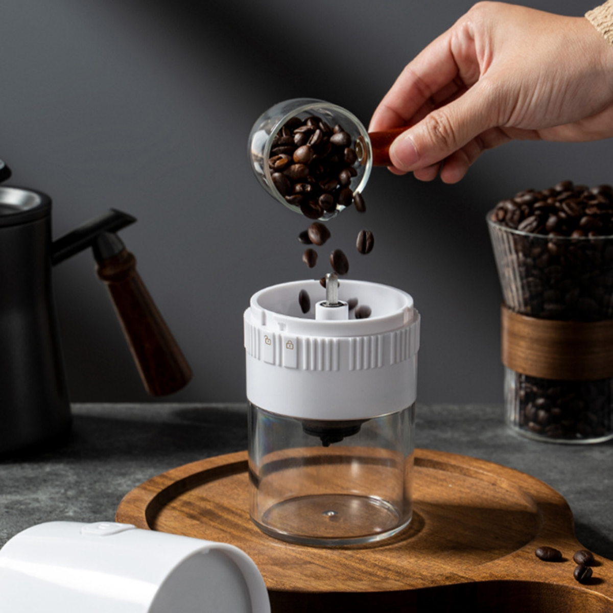 Eine Hand schüttet Kaffeebohnen in eine weiße Mühle. Ein Glas mit Bohnen ist hinten.