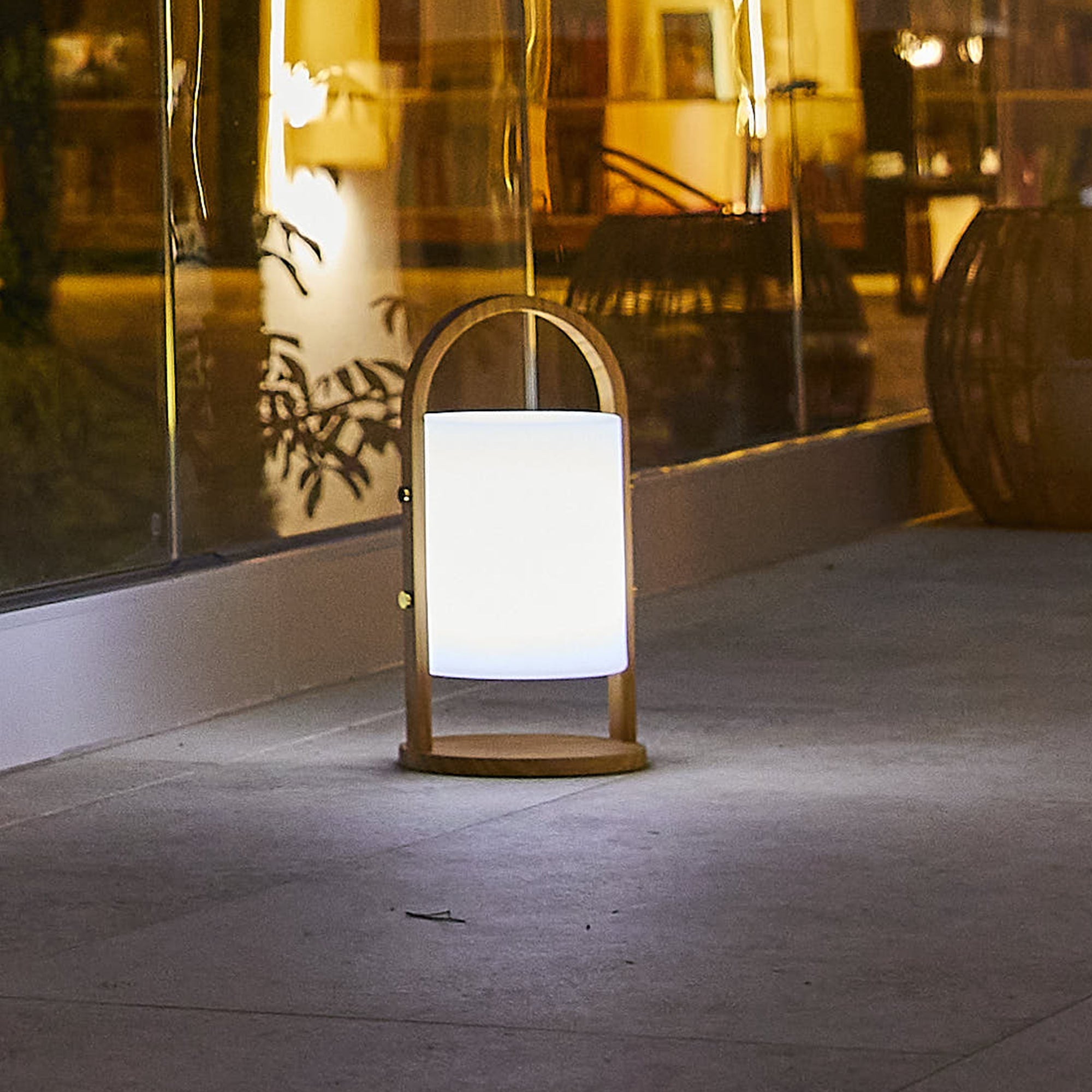 Eine Lampe auf einem Steinboden im Freien bei Nacht. Die Lampe ist weiß und hat einen Holzrahmen.