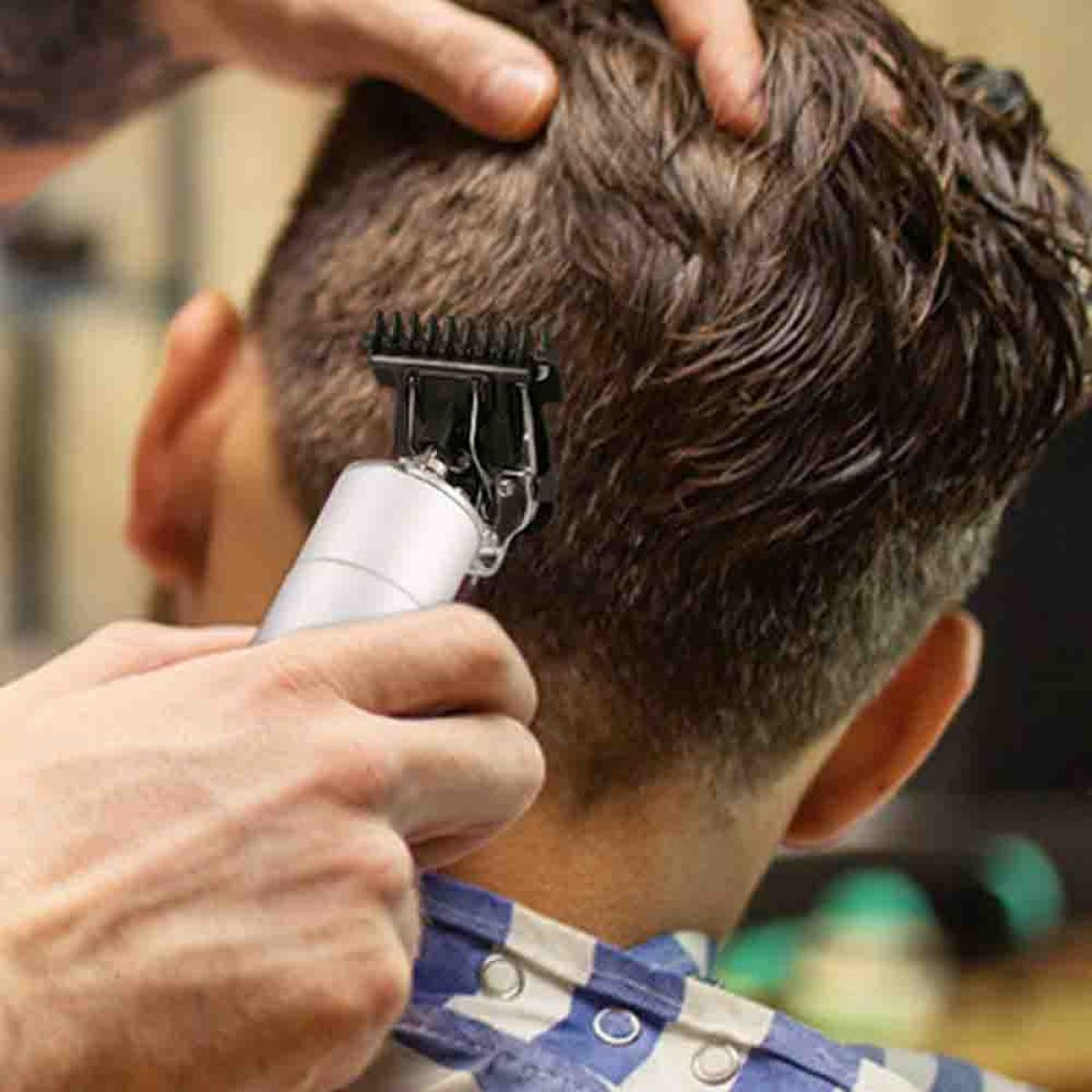 Eine Person schneidet mit einem elektrischen Haarschneider die Haare einer anderen Person.