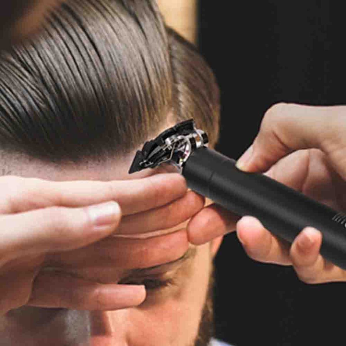 Eine Person schneidet Haare mit einem schwarzen Clipper. Das Haar ist braun.