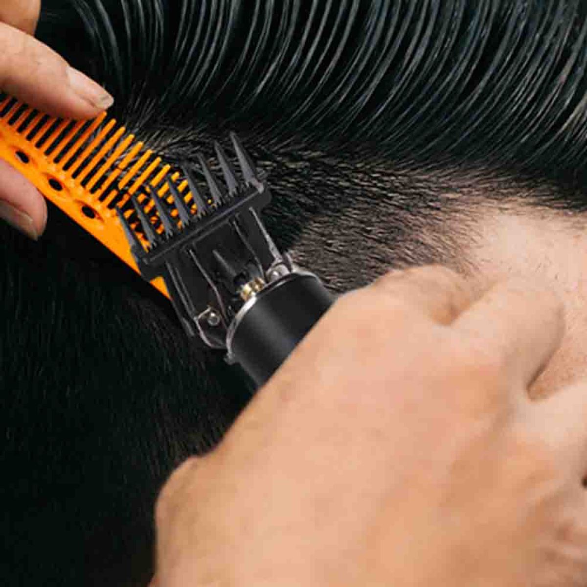 Nahaufnahme einer Person, die mit einem orangefarbenen und schwarzen Haarschneider dunkles Haar schneidet.