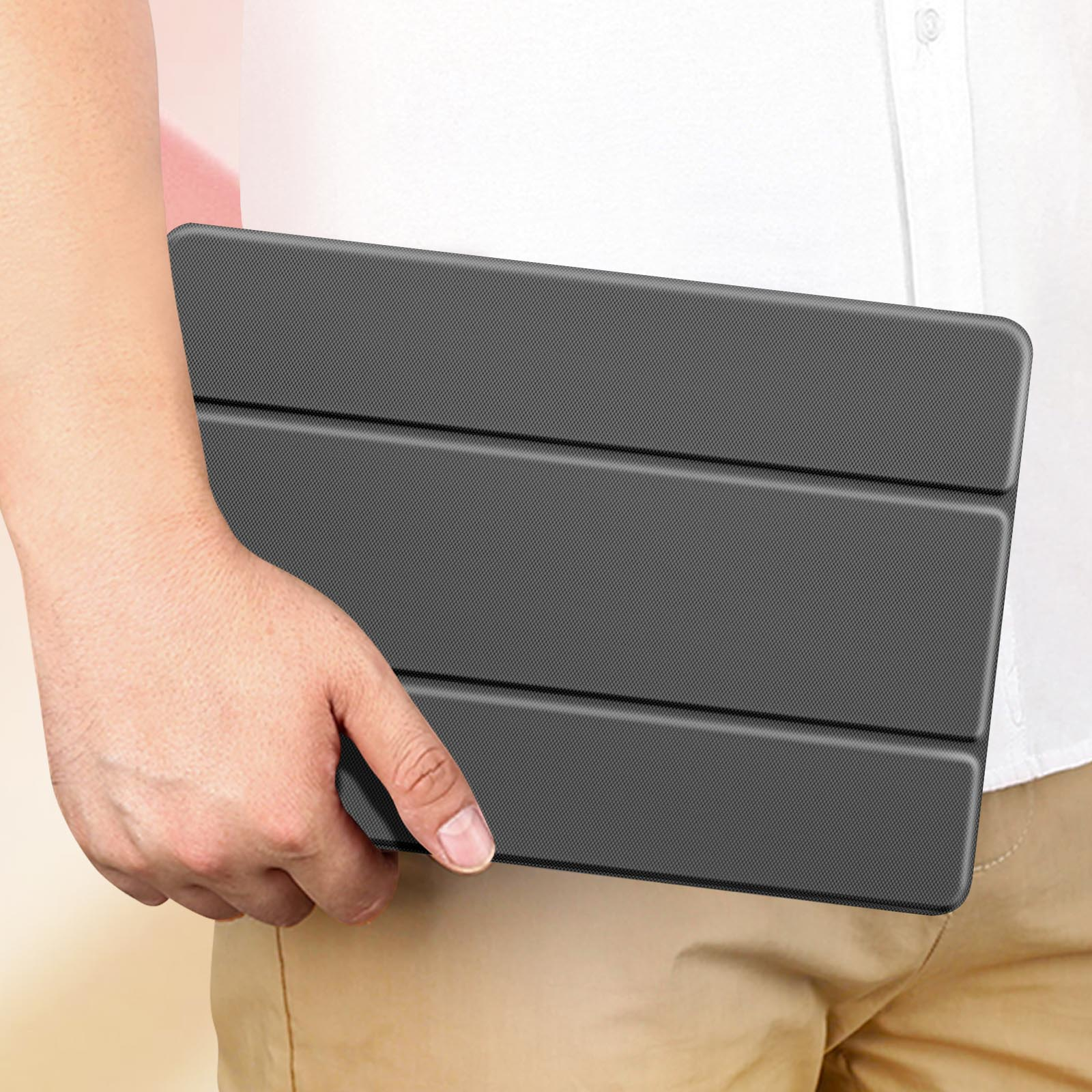 Una persona tiene in mano una custodia per tablet grigio scuro chiusa. Camicia bianca e pantaloni kaki.
