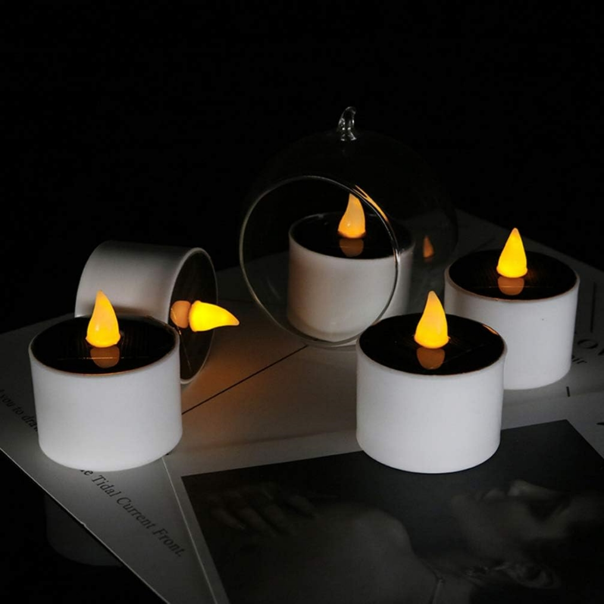 Vier weiße Kerzen mit gelben Flammen auf einem Tisch, dunkler Hintergrund.