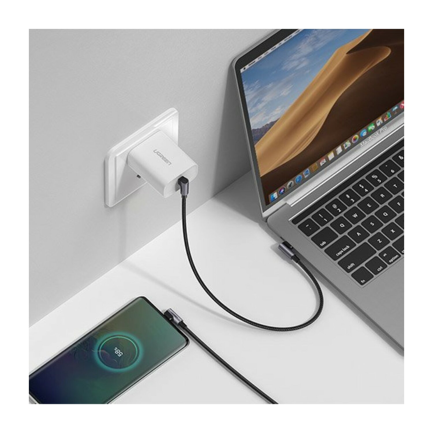 Telefon ładuje się obok laptopa. Ładowarka jest podłączona do ściany.