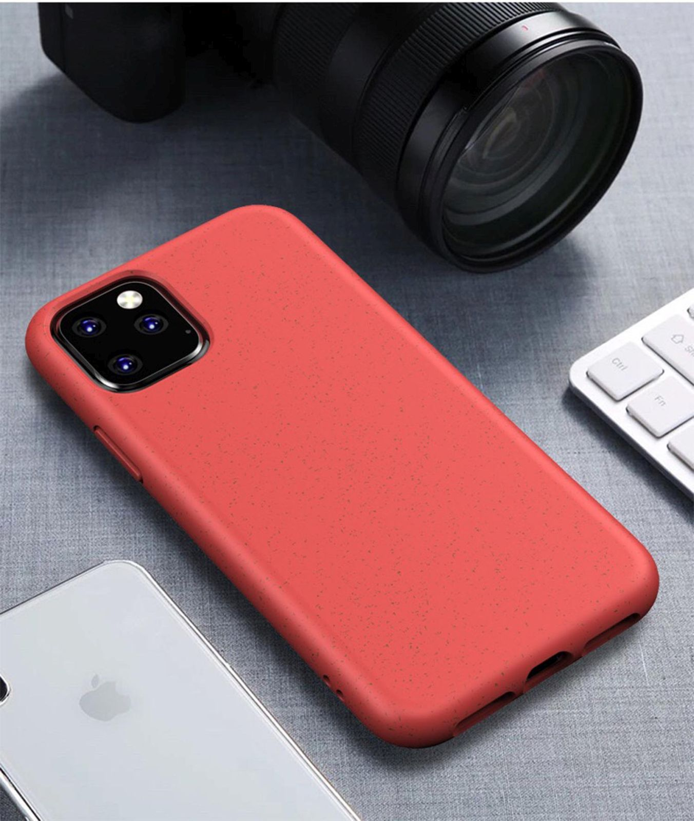 Rote Handyhülle auf einem Tisch, ein Telefon, eine Kamera im Hintergrund und eine Tastatur.