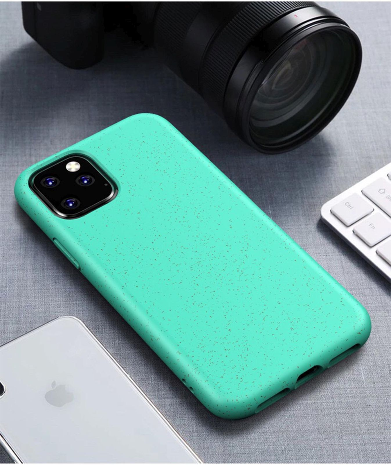 Eine türkisfarbene Handyhülle mit Kamera, weiße Tastatur und ein weißes Handy auf grauem Untergrund.
