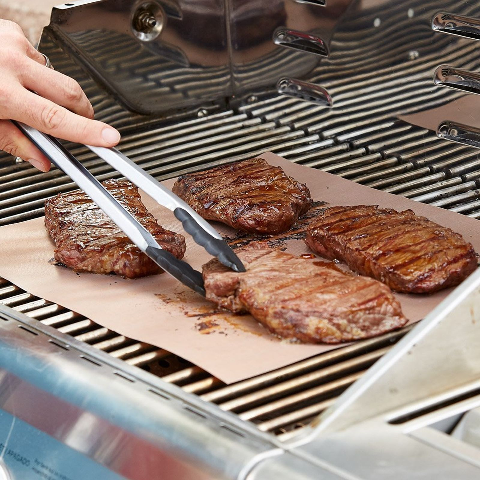 Person grillt Steaks auf einem Grill, benutzt Zangen.
