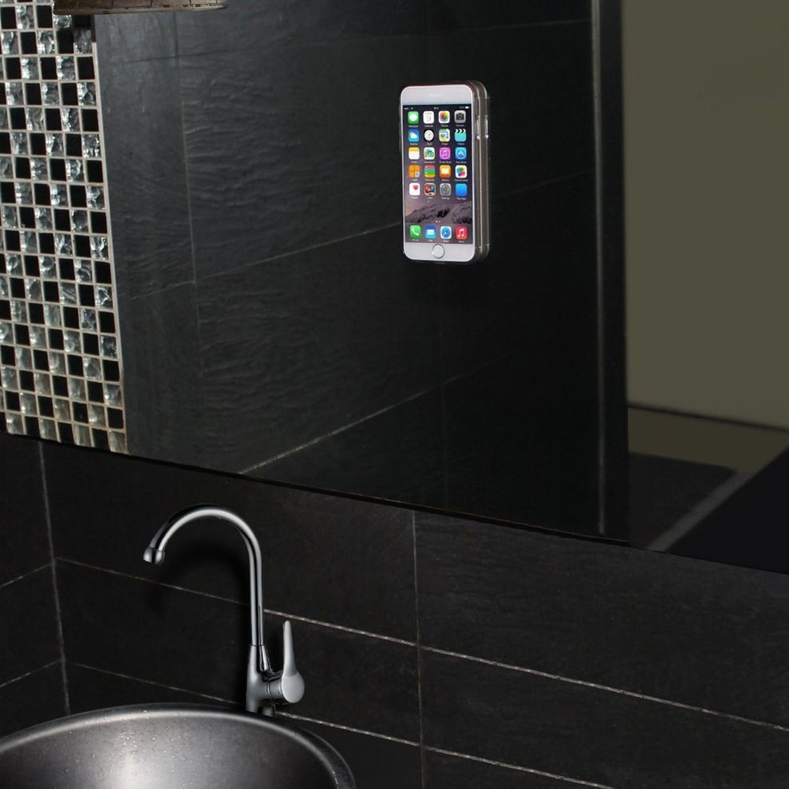 Ein Telefon ist an einer schwarzen Fliesenwand montiert und spiegelt sich in einem Spiegel über einem Waschbecken.