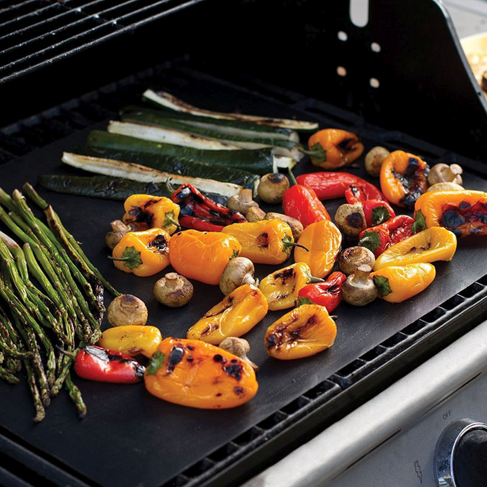Gegrilltes Gemüse, darunter Paprika und Zucchini, auf einer schwarzen Grillfläche.