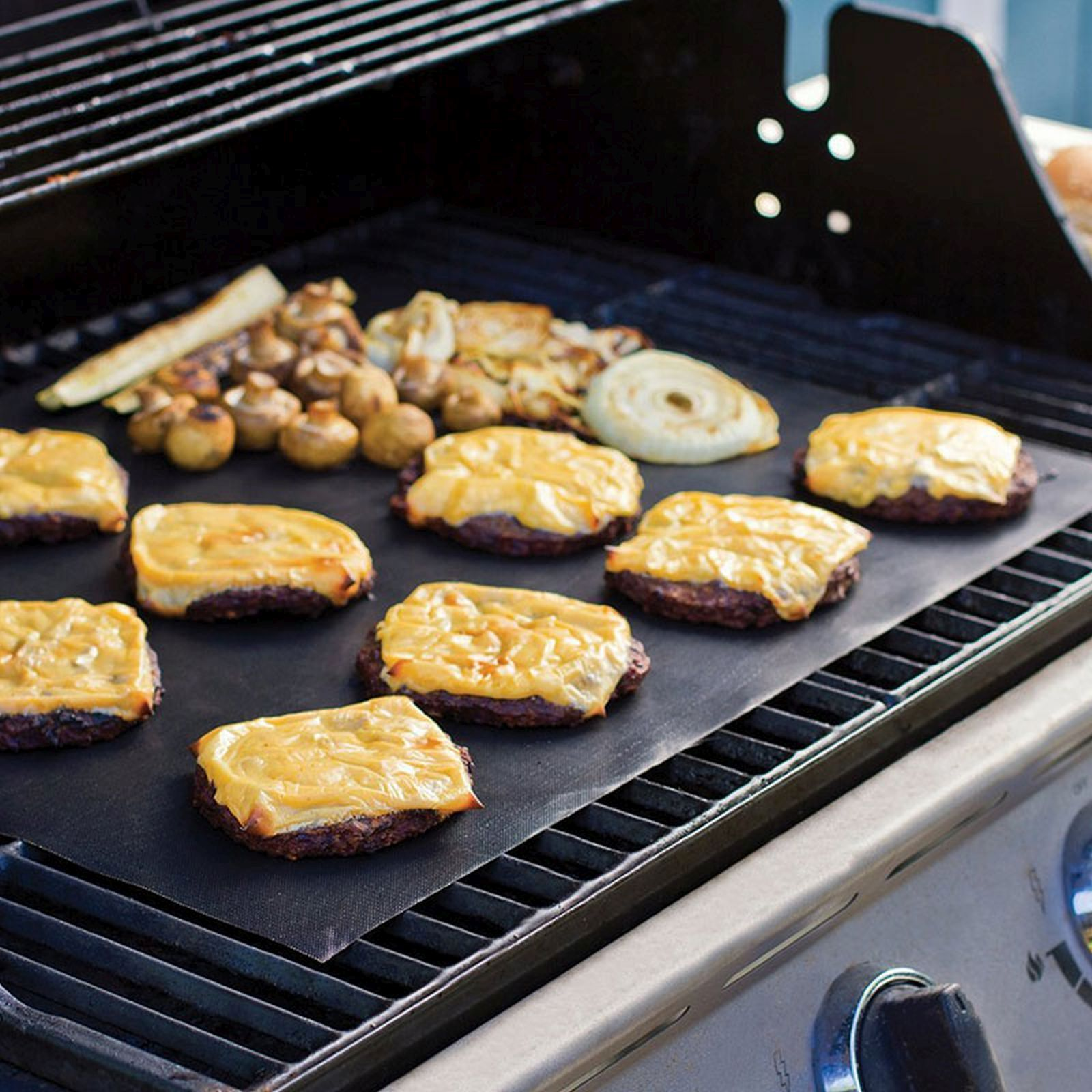 Burger mit Käse auf einer schwarzen Grillmatte, daneben gegrilltes Gemüse.