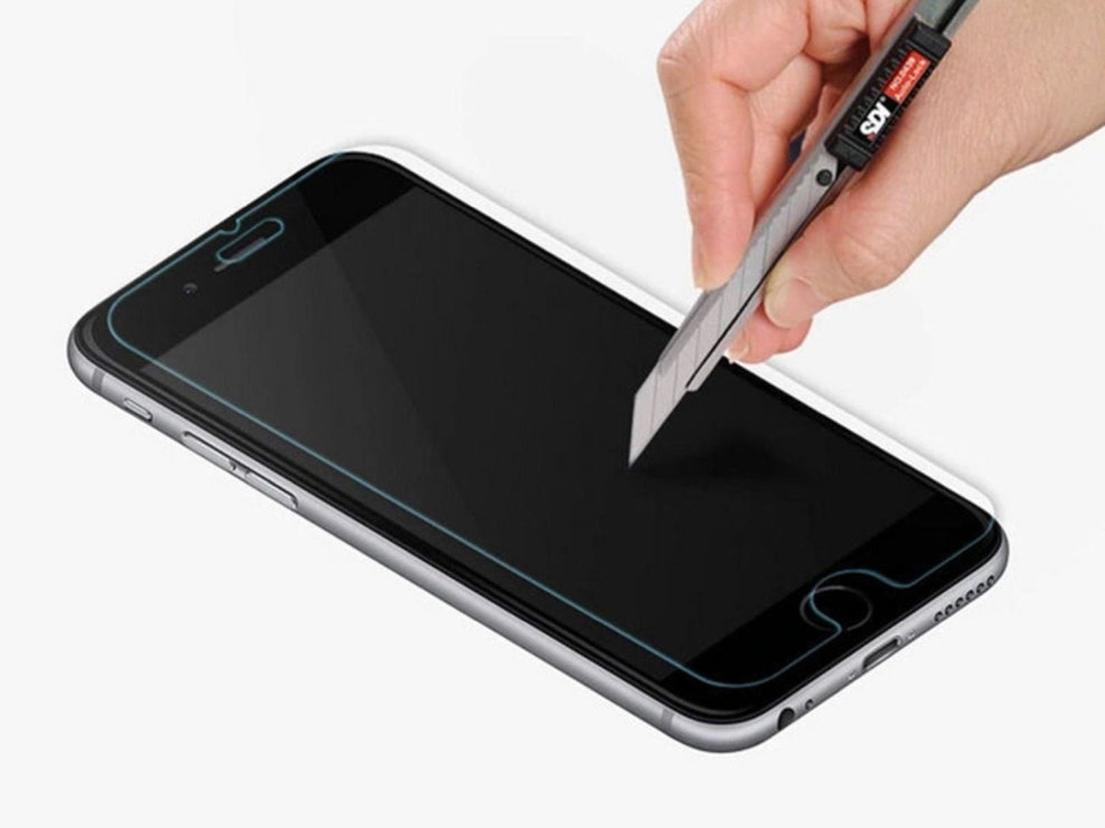 Eine Person schneidet eine Displayschutzfolie mit einem Rasierer auf einem Telefon zu. Das Telefon liegt auf einer weißen Oberfläche.