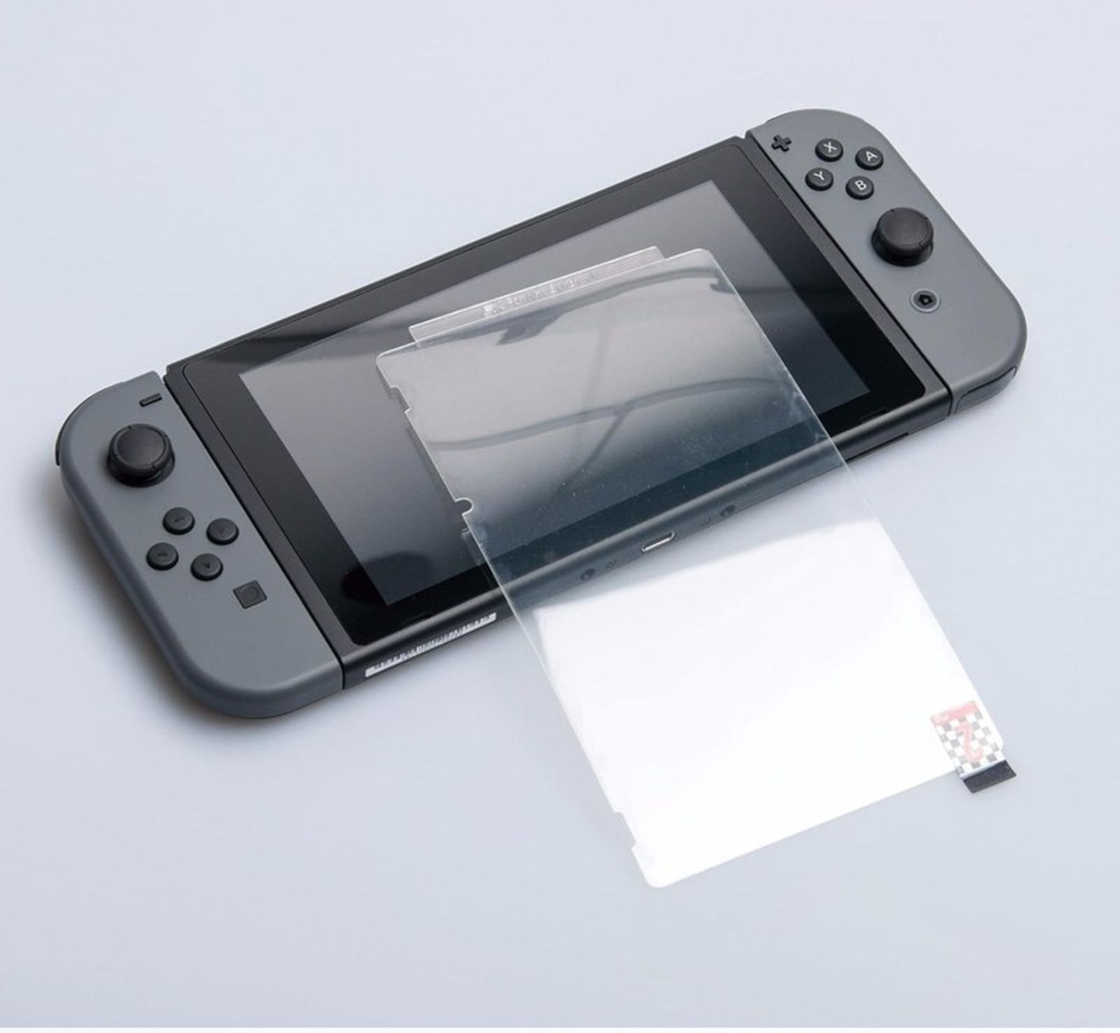 Nintendo Switch mit Displayschutz. Graue Joy-Cons angebracht. Weiße Oberfläche.