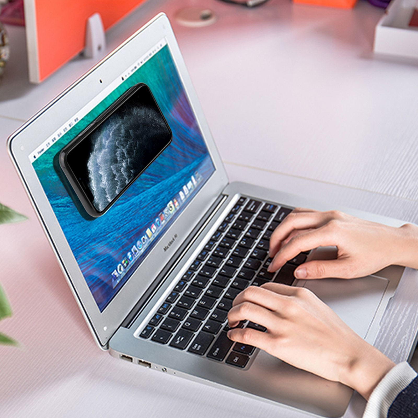 Hände tippen auf einer Laptop-Tastatur; ein Telefon wird auf dem Bildschirm angezeigt.