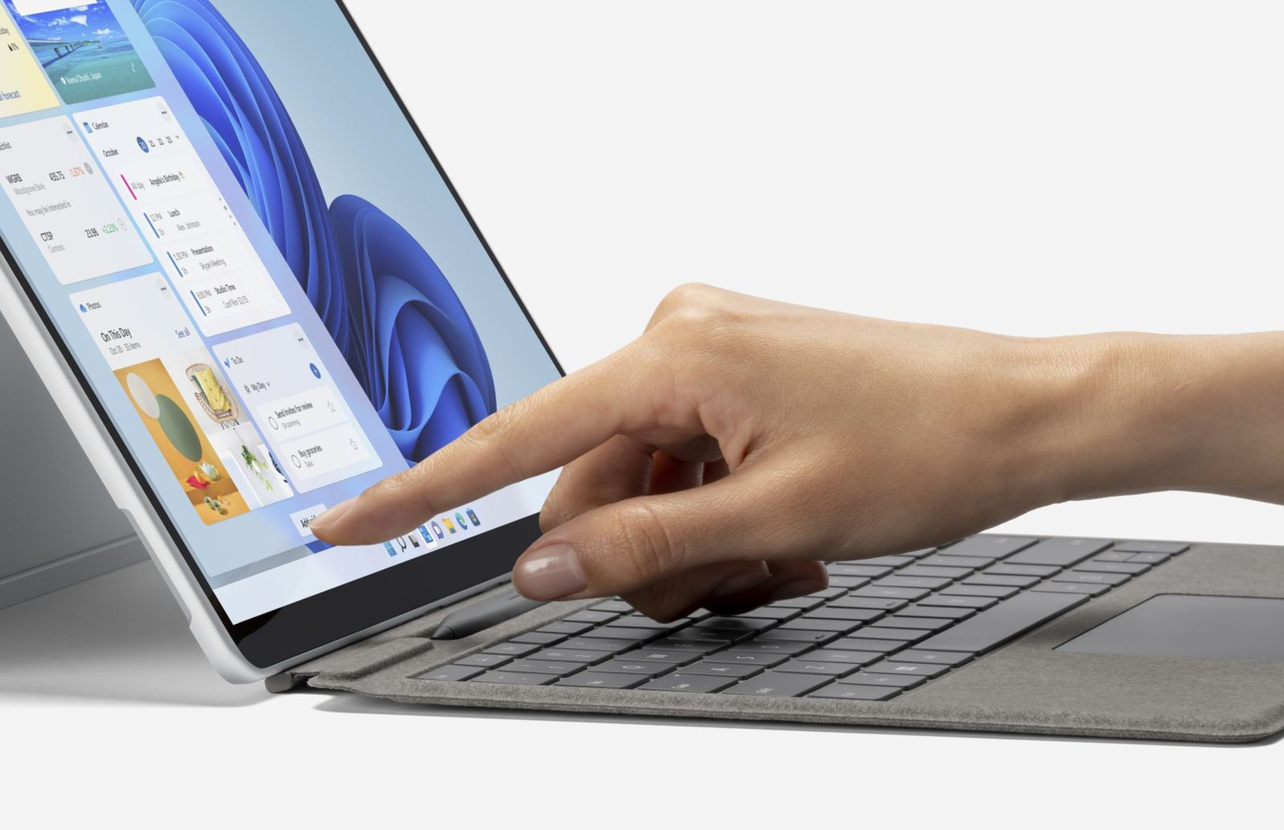 Una mano tocca lo schermo di un laptop che mostra i widget, con una tastiera in primo piano.