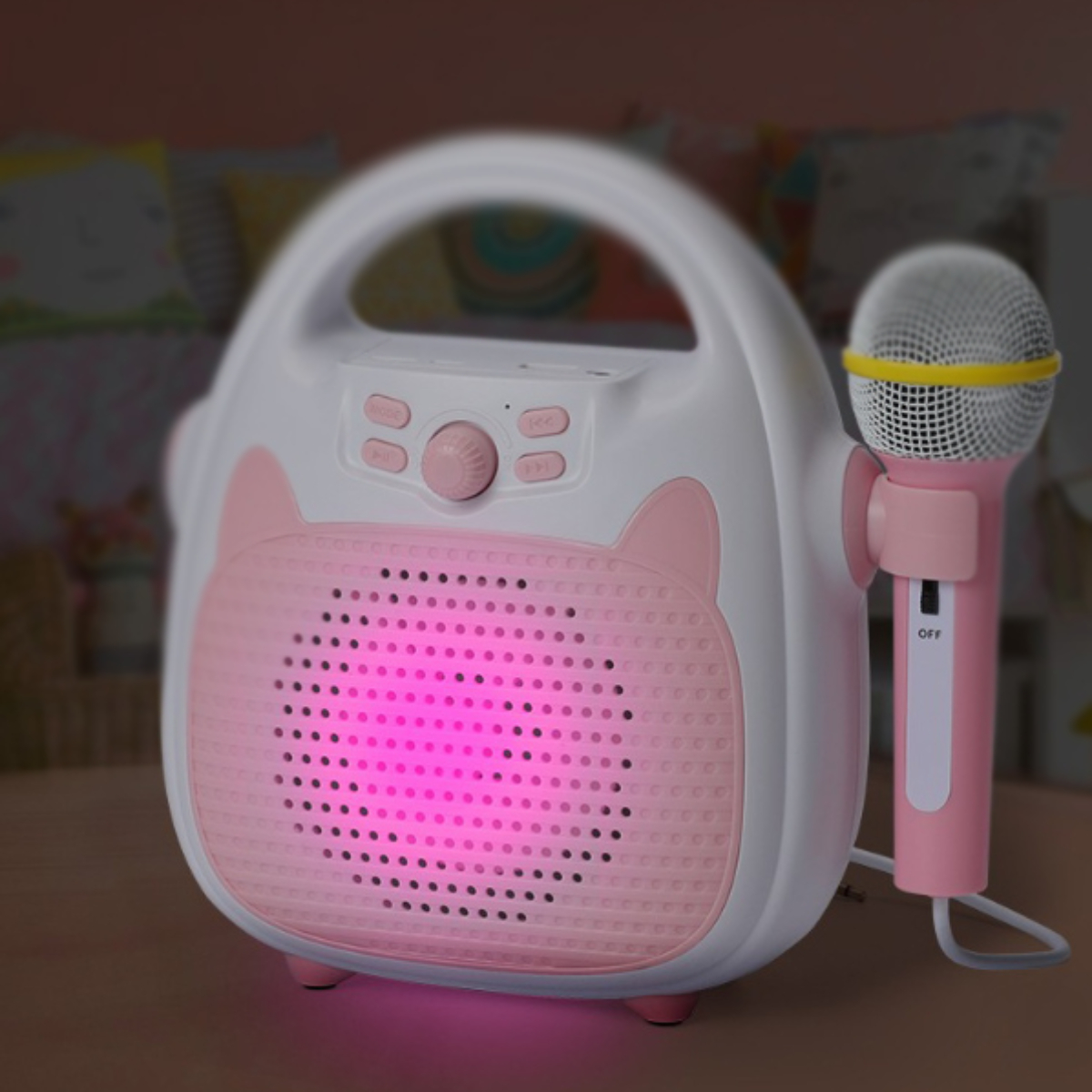 Eine weiß-rosa Karaoke-Maschine mit Mikrofon, vor einem verschwommenen rosa-weißen Hintergrund.