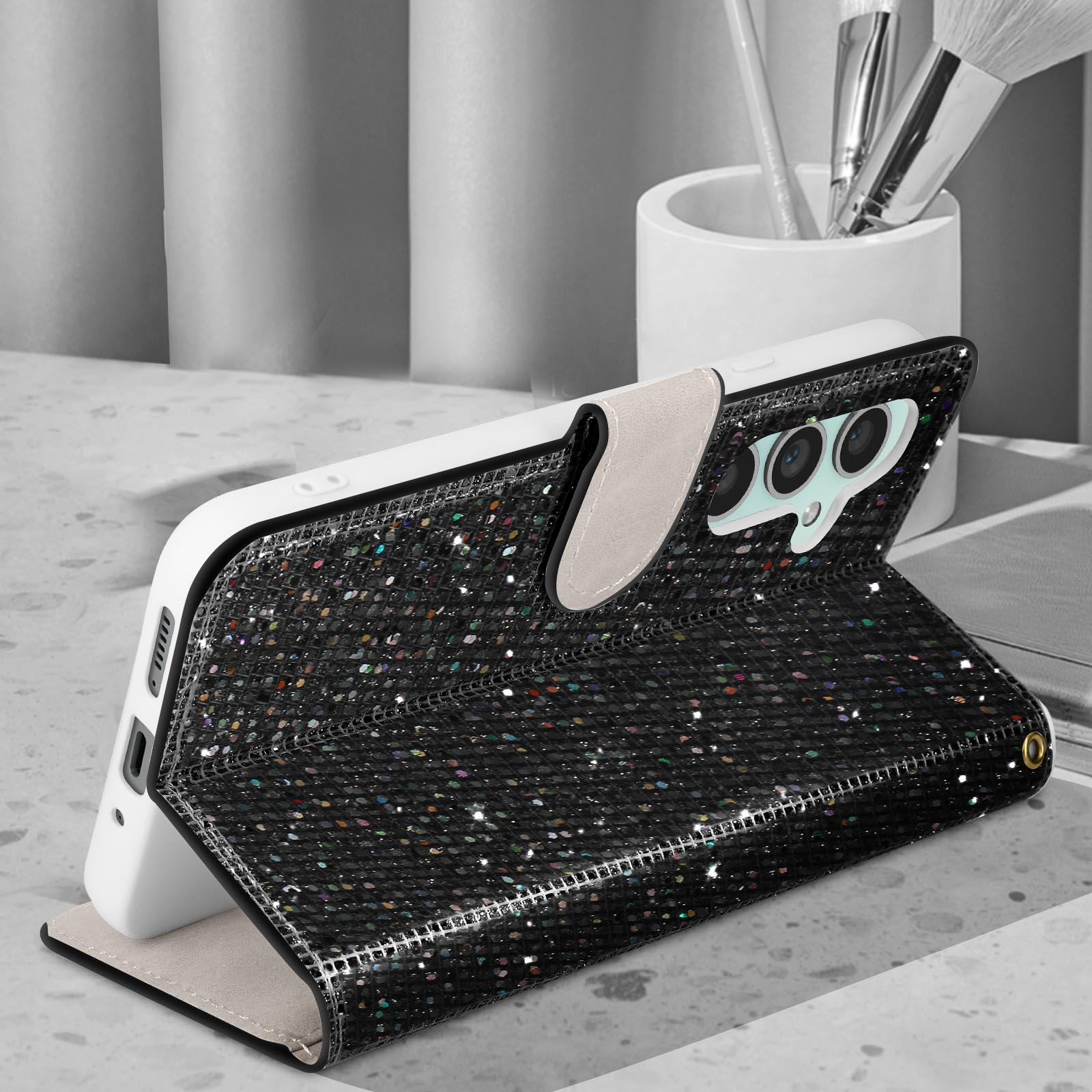 Custodia per telefono con design glitterato, aperta. Un telefono è dentro. Su una scrivania.