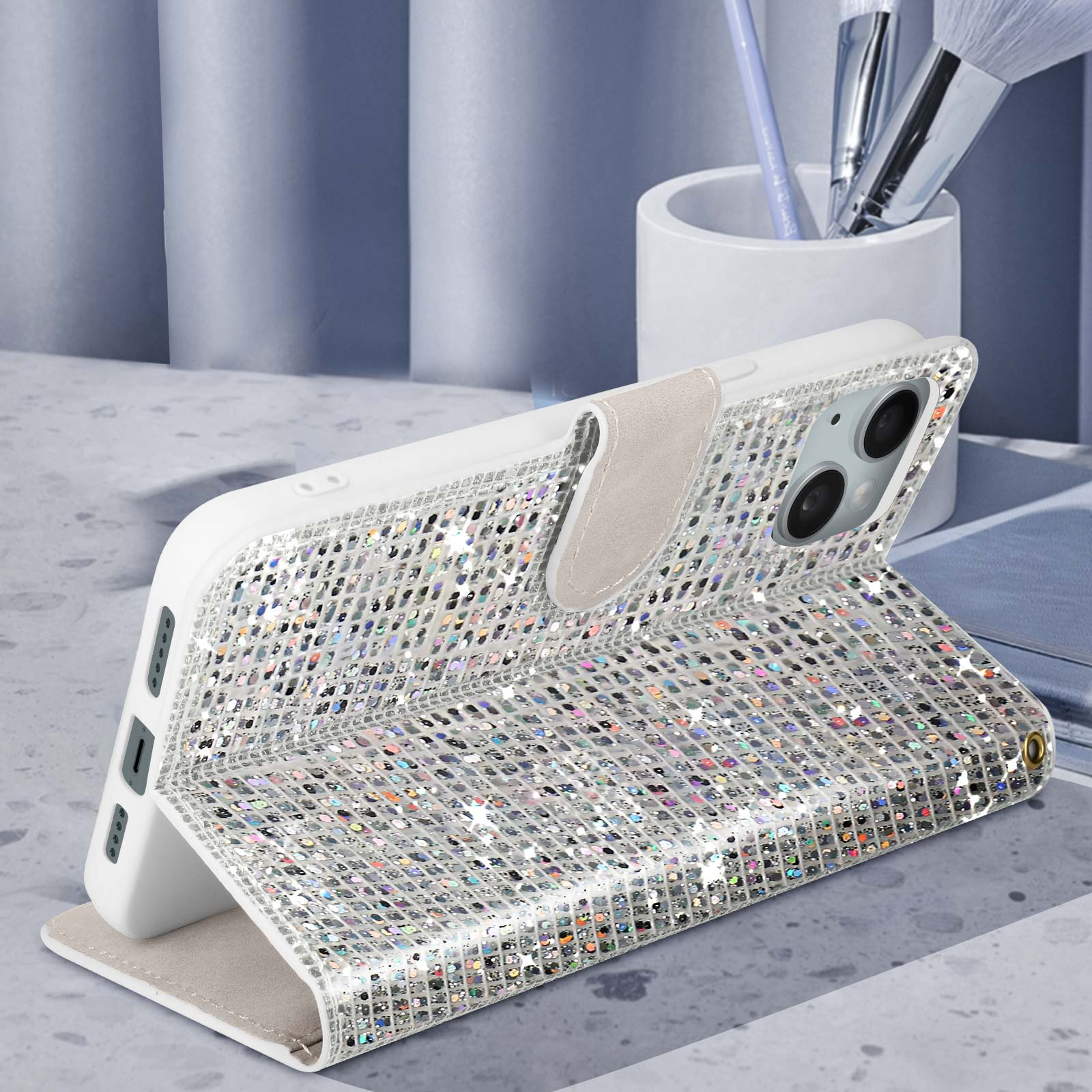 Custodia per telefono argento aperta con dettagli scintillanti. Sfondo bianco e pennelli per trucco sullo sfondo.