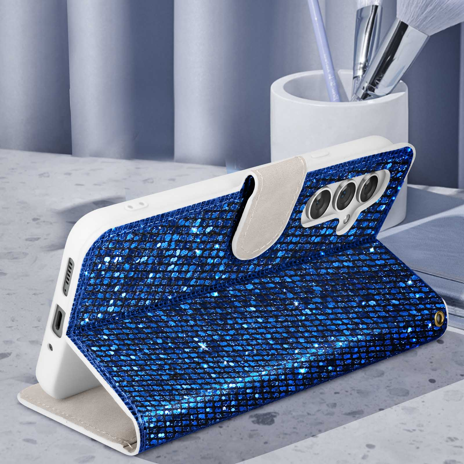 Una custodia blu scintillante, aperta, che mostra un telefono. Pennelli per trucco in una tazza bianca.