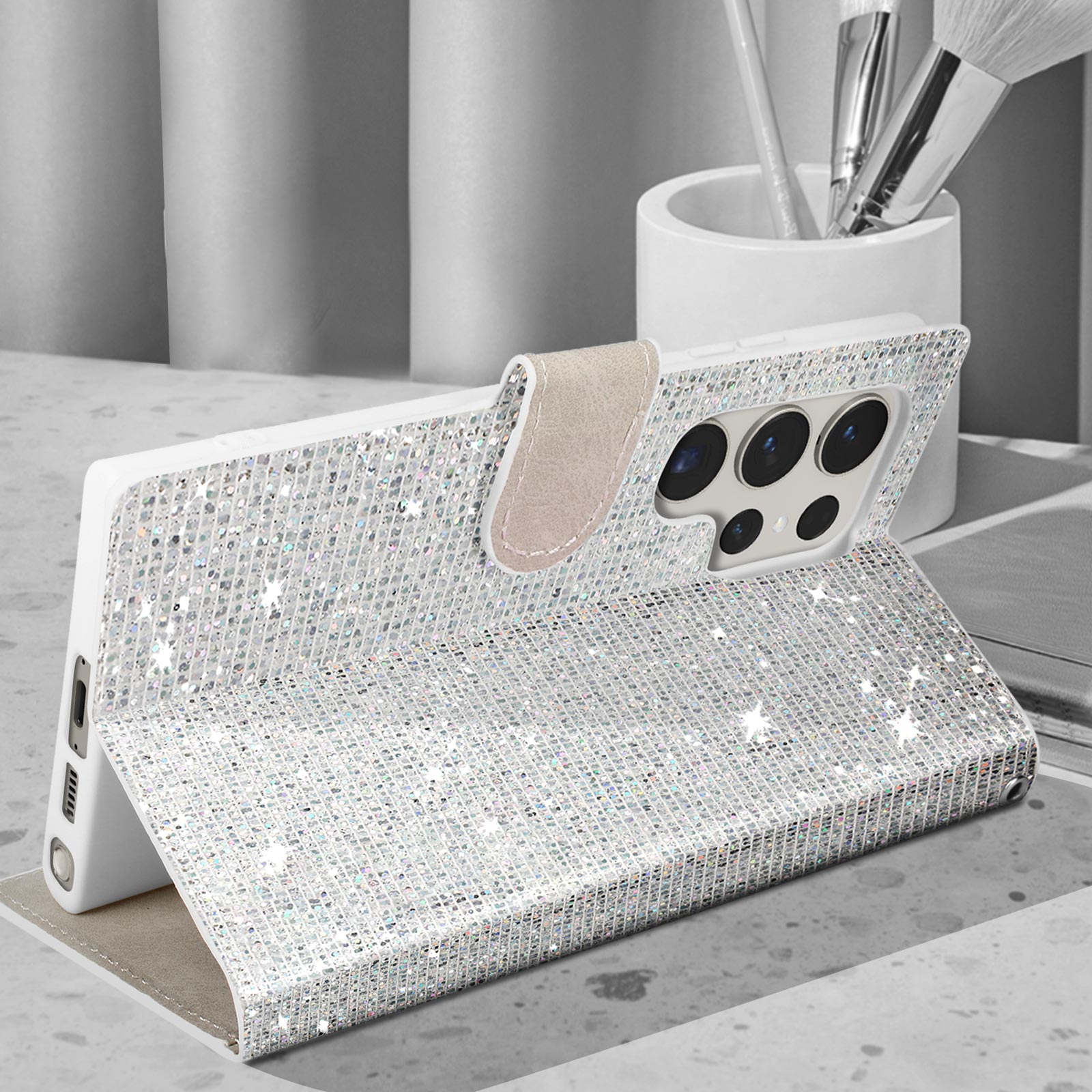 Custodia per telefono glitterata, aperta per rivelare il telefono. Pennelli trucco e contenitore sullo sfondo.